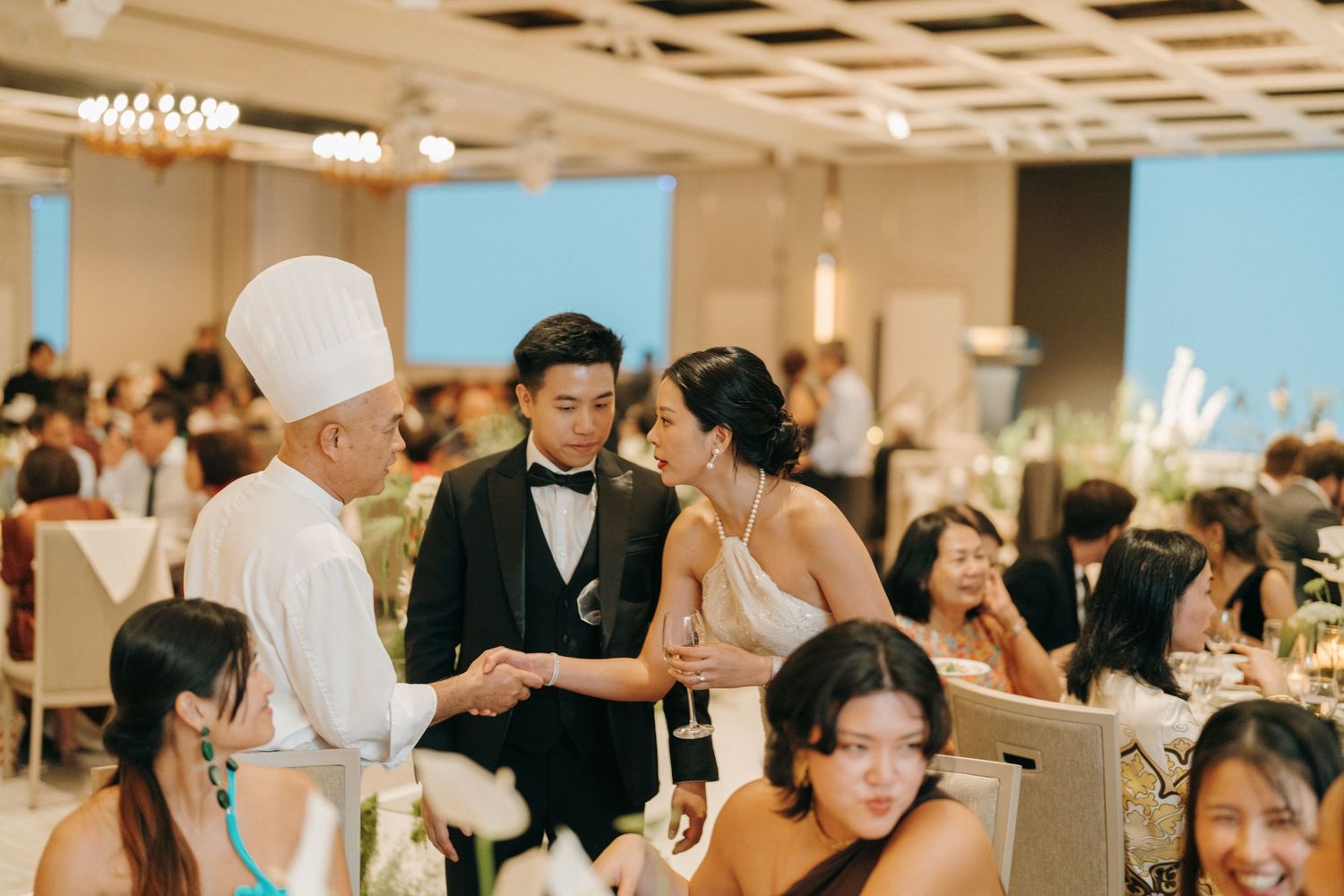 Wedding reception guests enjoying a celebration in an elegant indoor venue with decorative ceiling details.