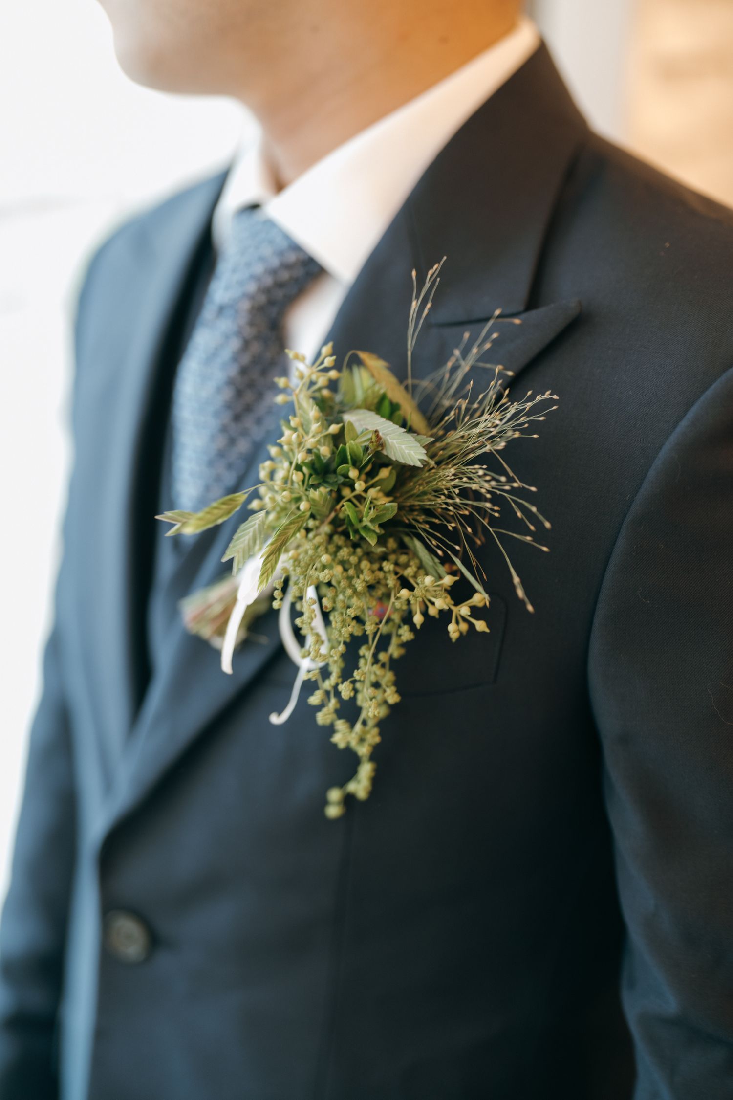 Row of groomsmen's boutonnieres featuring delicate green foliage on navy suits.