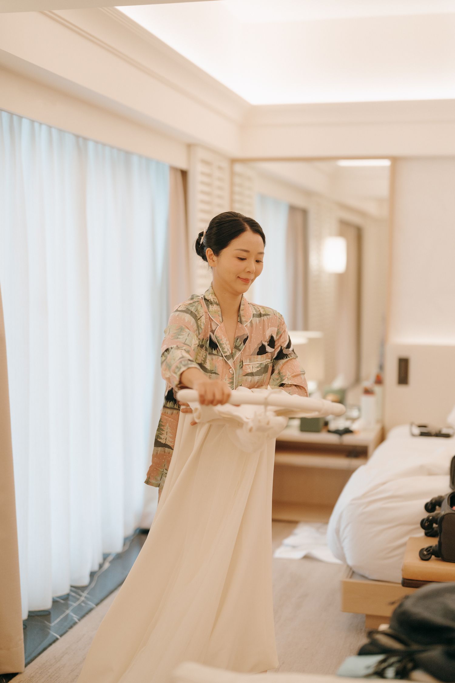 A person in a floral print jacket carefully handling a white wedding dress in a bridal suite.