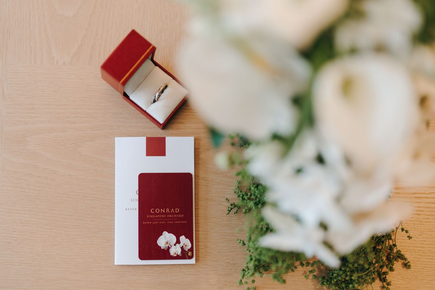 Red wedding ring box and invitation card styled with delicate white flowers.