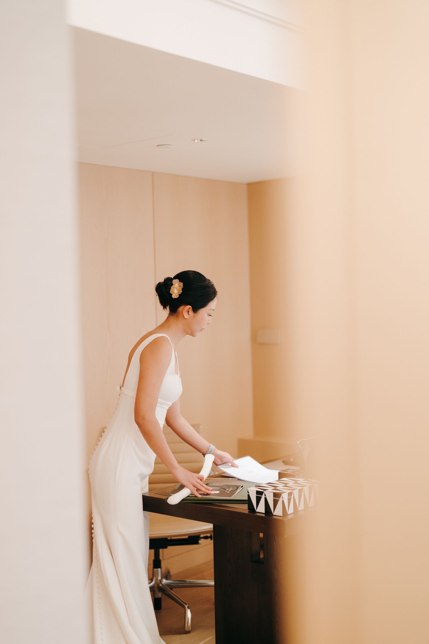 A person in a white dress arranging items on a dark table in a minimalist room.