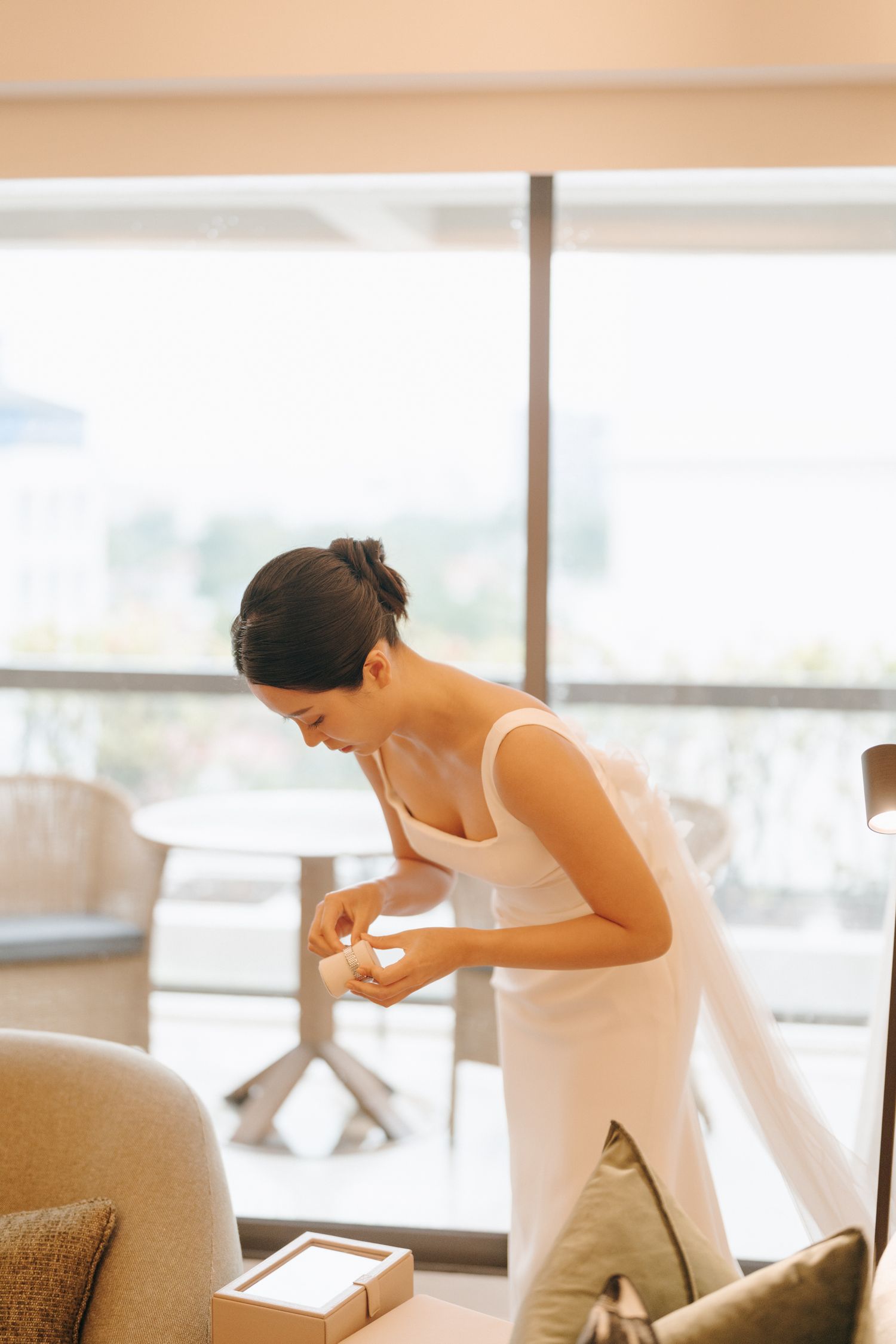 Someone in a white dress leaning over to examine something in a bright modern room.