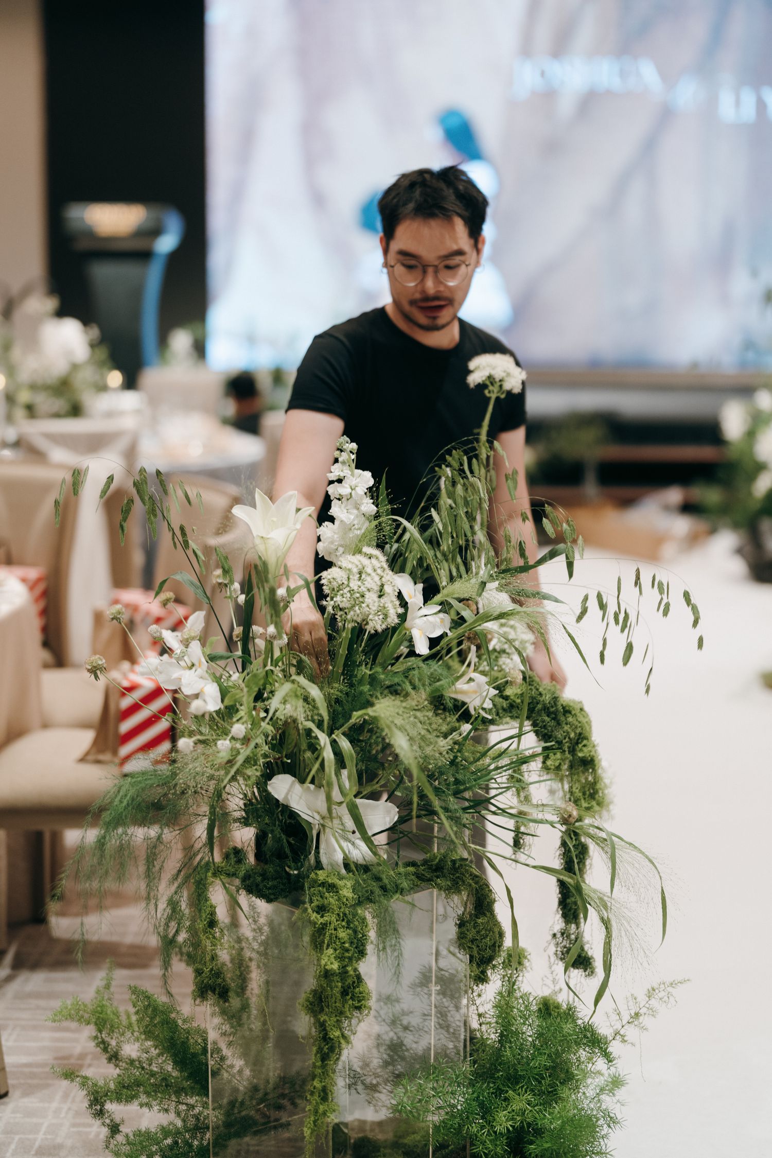 Event florist arranging lush white floral centerpieces with cascading greenery in an elegant reception space.