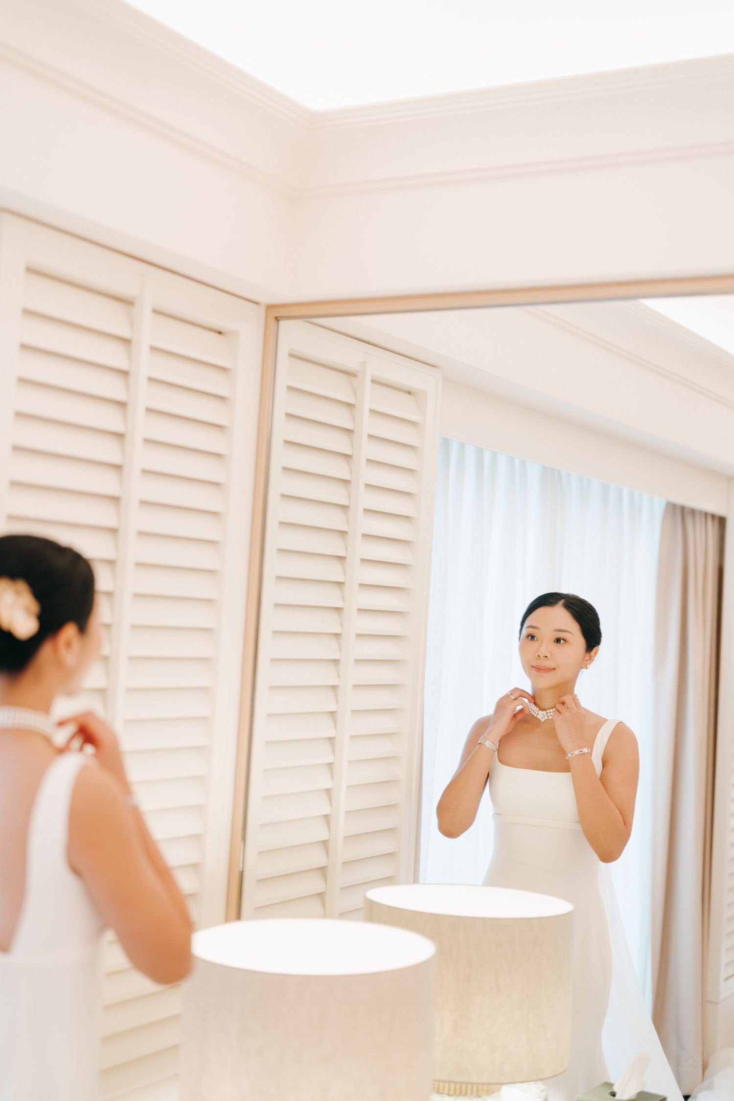 Elegant bridal preparation scene with white shutters and mirror reflection.