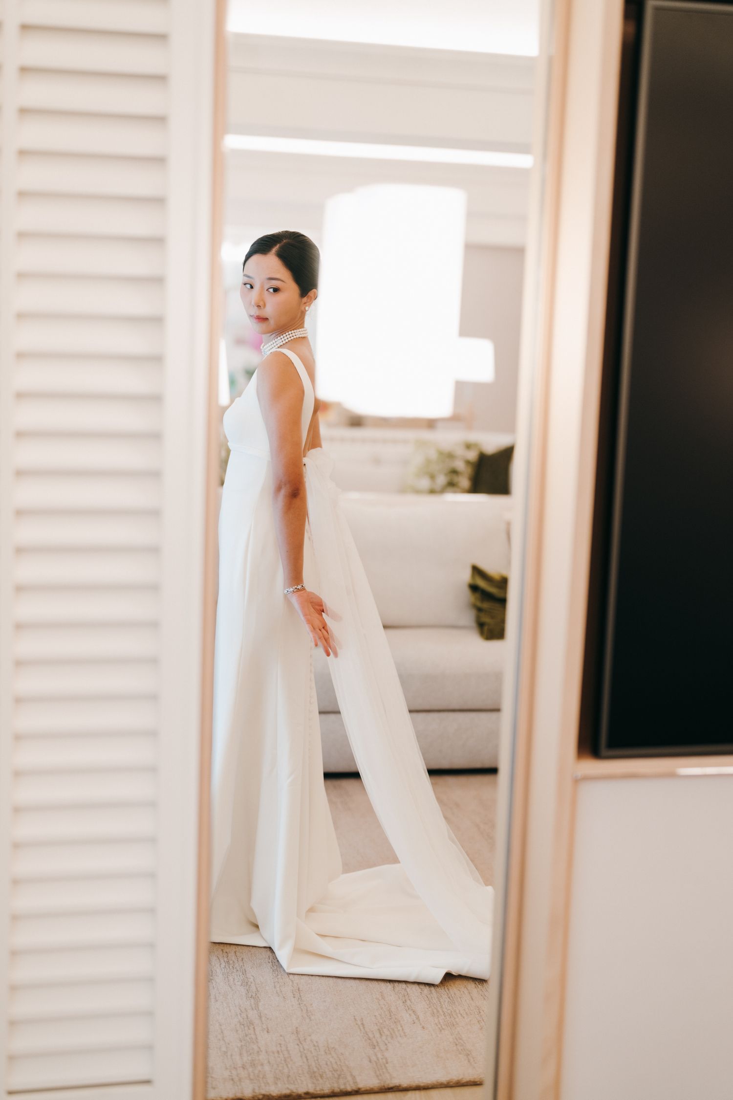 Elegant white wedding dress reflected in mirror with louvered doors.