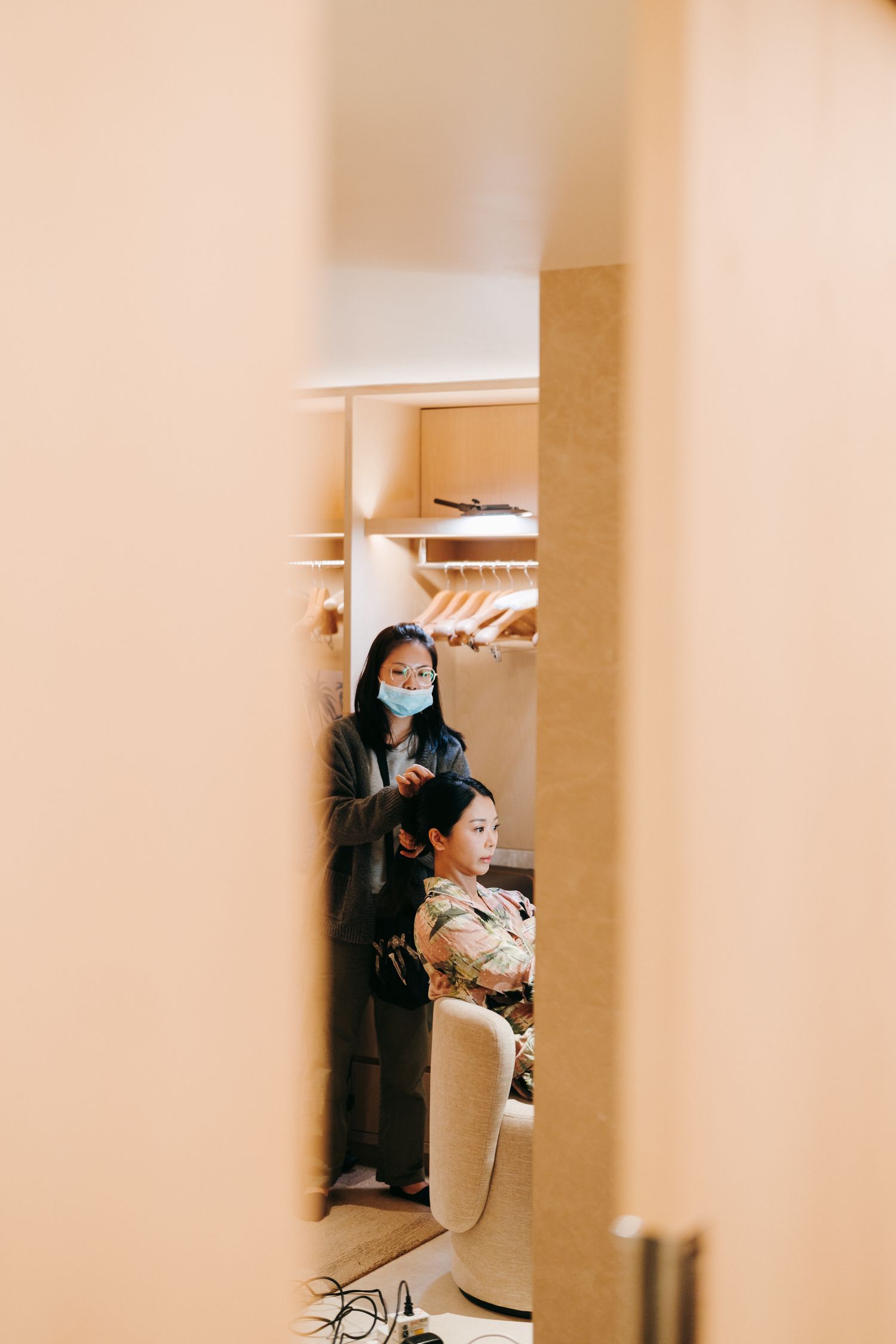 A glimpse through a doorway showing someone in a face mask standing in a dressing room with clothing racks.
