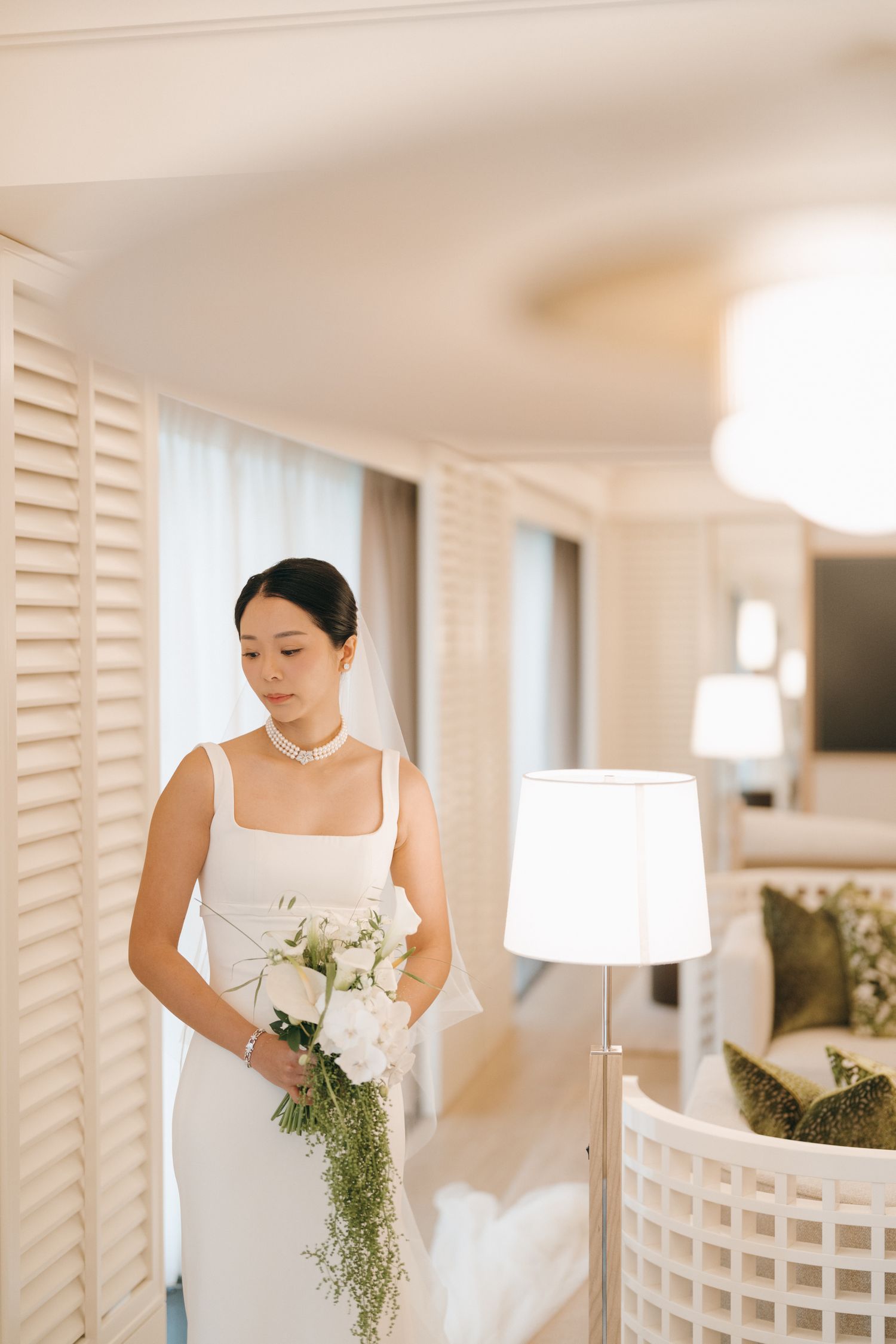 A person in a white wedding dress holds a bouquet of white flowers with cascading greenery in an elegant room.