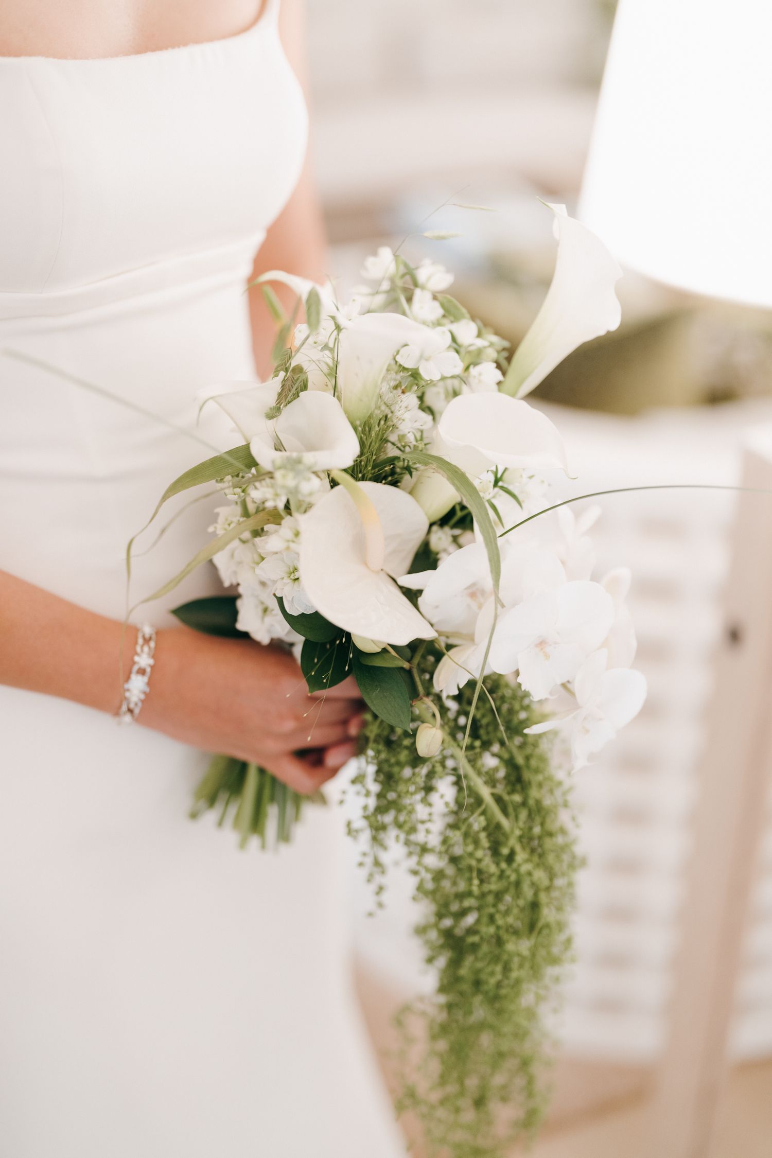 A delicate white bridal bouquet with cascading greenery and small flowers held against a light background.