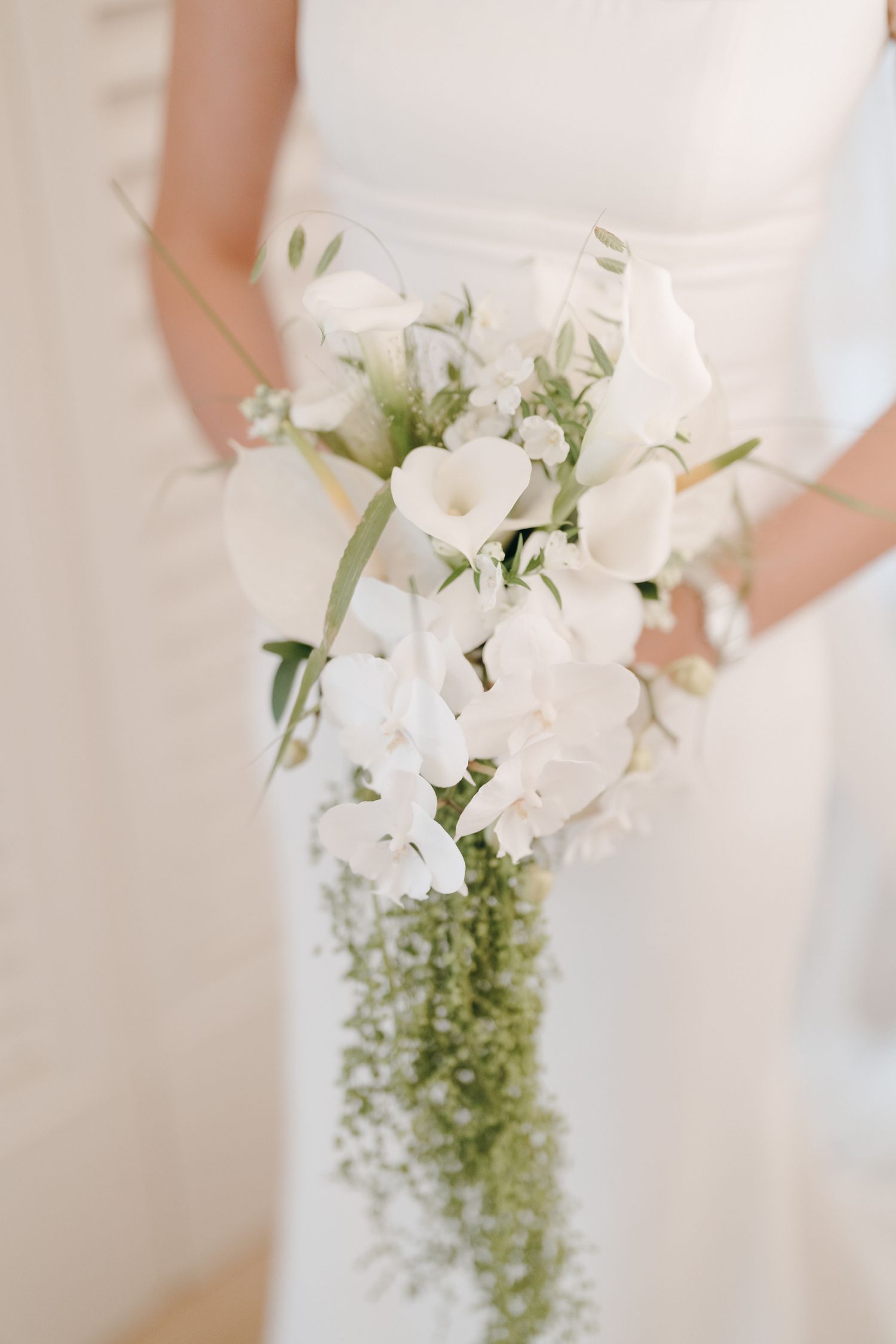 Elegant white bridal bouquet with delicate flowers and greenery against a light background.