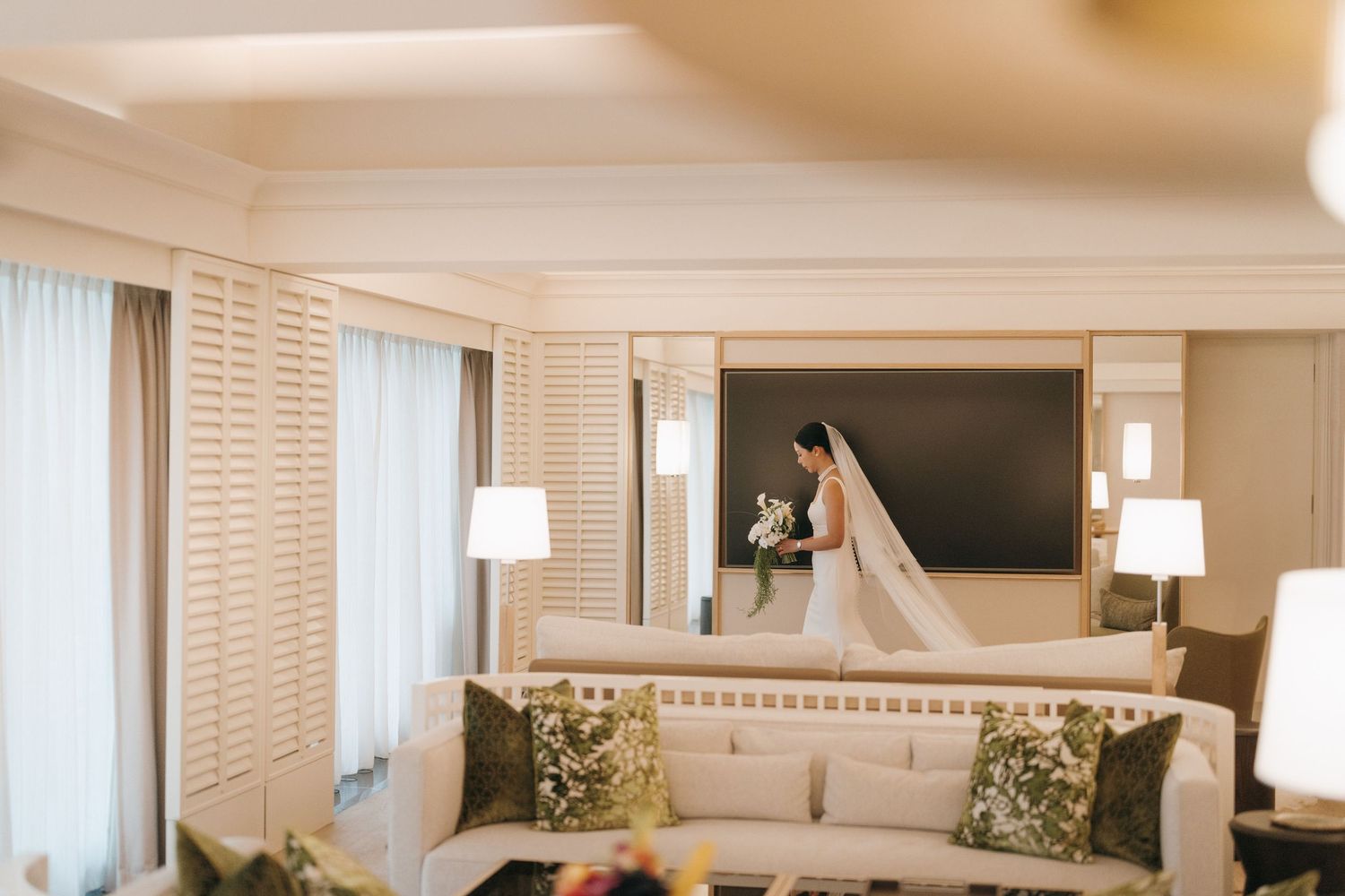 An elegant hotel ballroom with white shuttered windows, crown molding, and modern wall sconces.