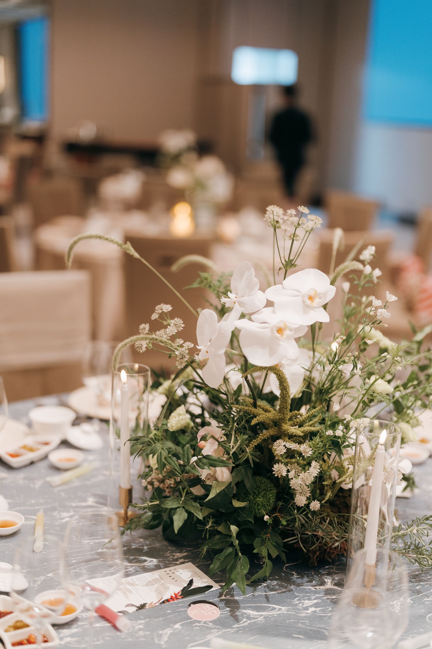 White orchid and greenery centerpiece on a formal dining table with glassware and place settings.
