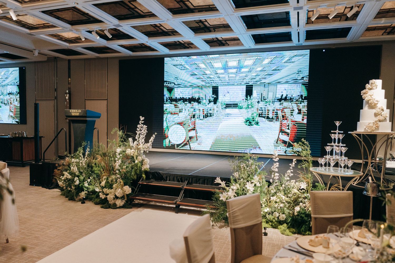 An elegant wedding reception venue with white floral centerpieces and modern lighting fixtures overhead.