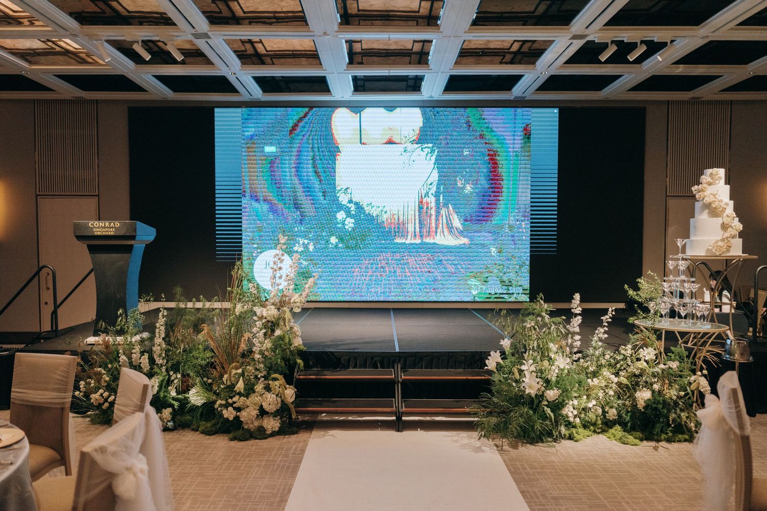 Event space with projection screen and lush floral arrangements decorating the stage area.