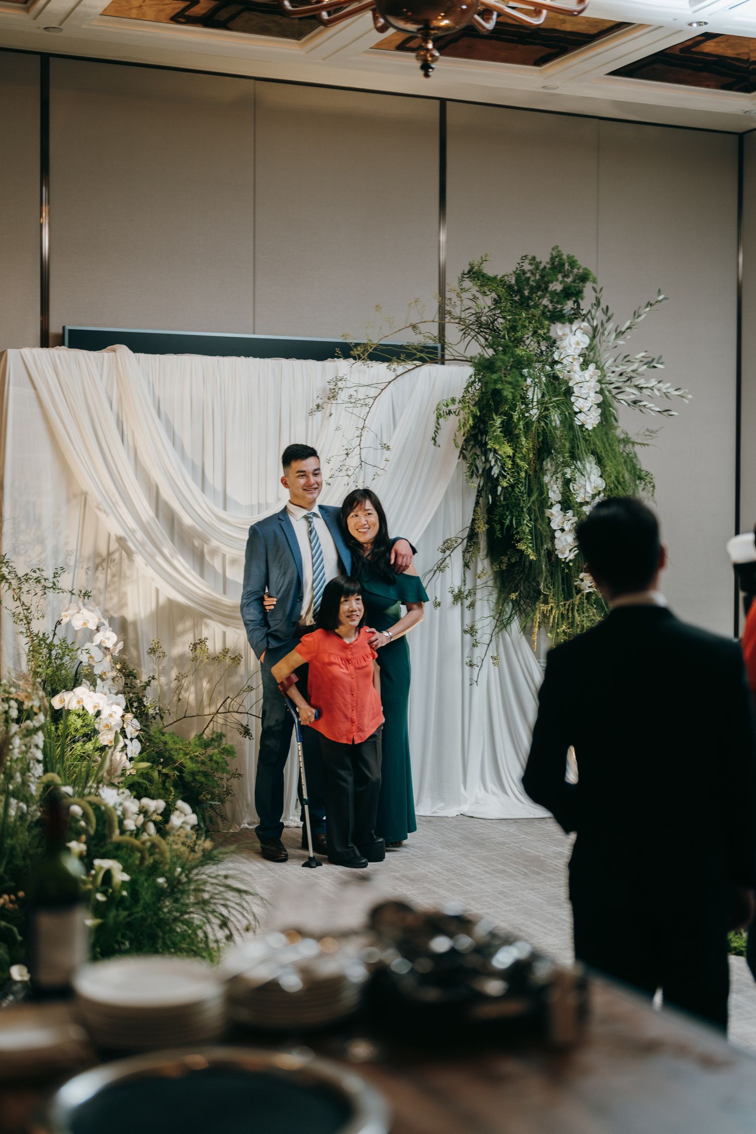 A family poses together in front of an elegant white backdrop with floral arrangements and greenery at an event.