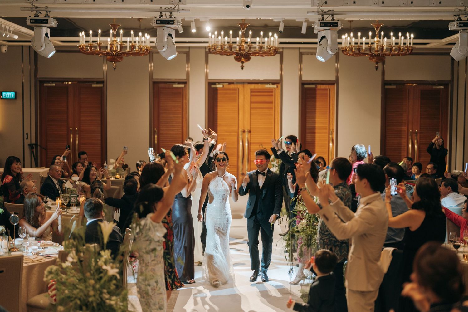 Wedding guests dance and celebrate on an elegant ballroom dance floor under crystal chandeliers at an evening reception.