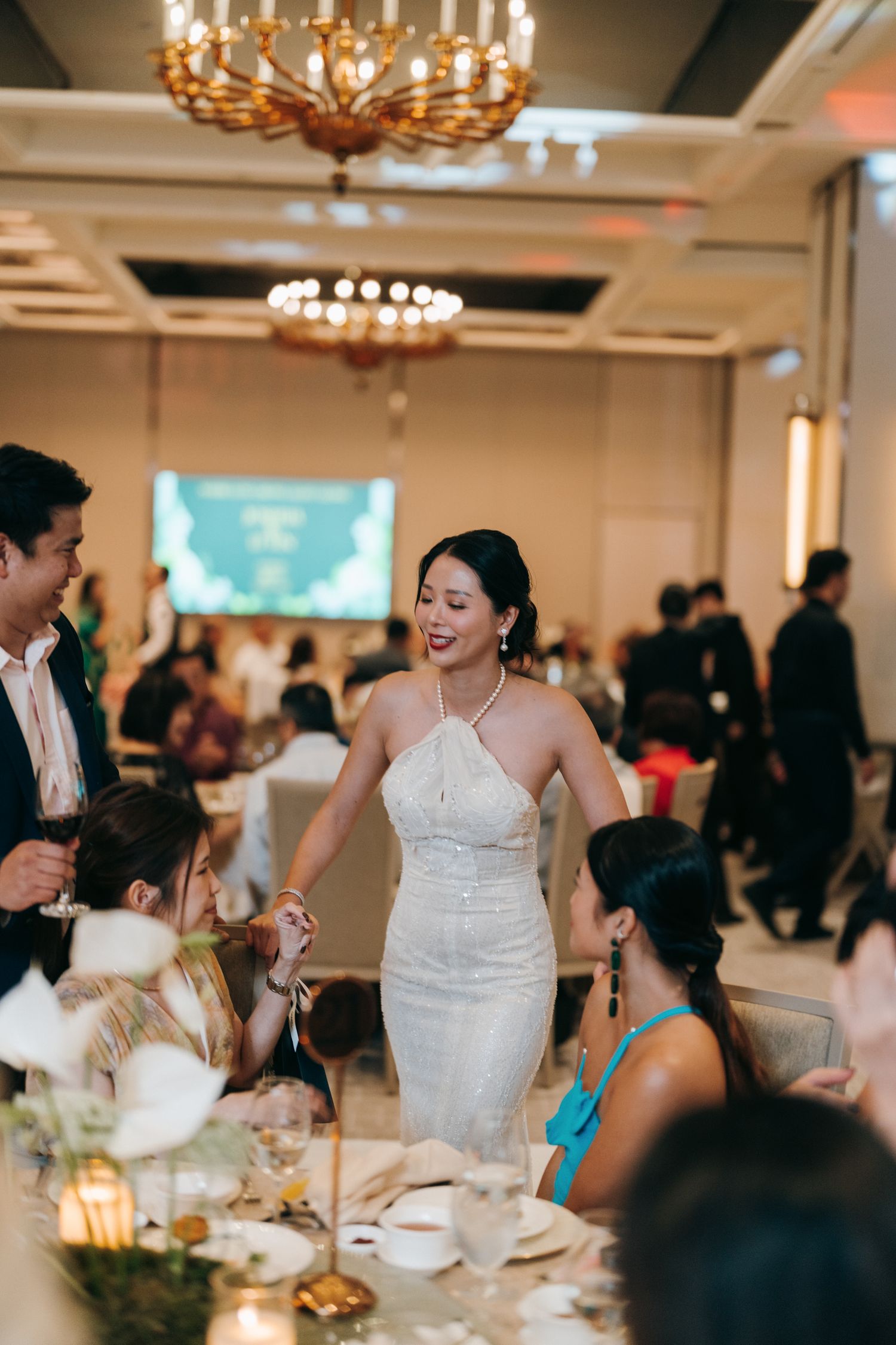 Elegant wedding reception in a ballroom with ornate chandeliers and guests mingling at decorated tables.