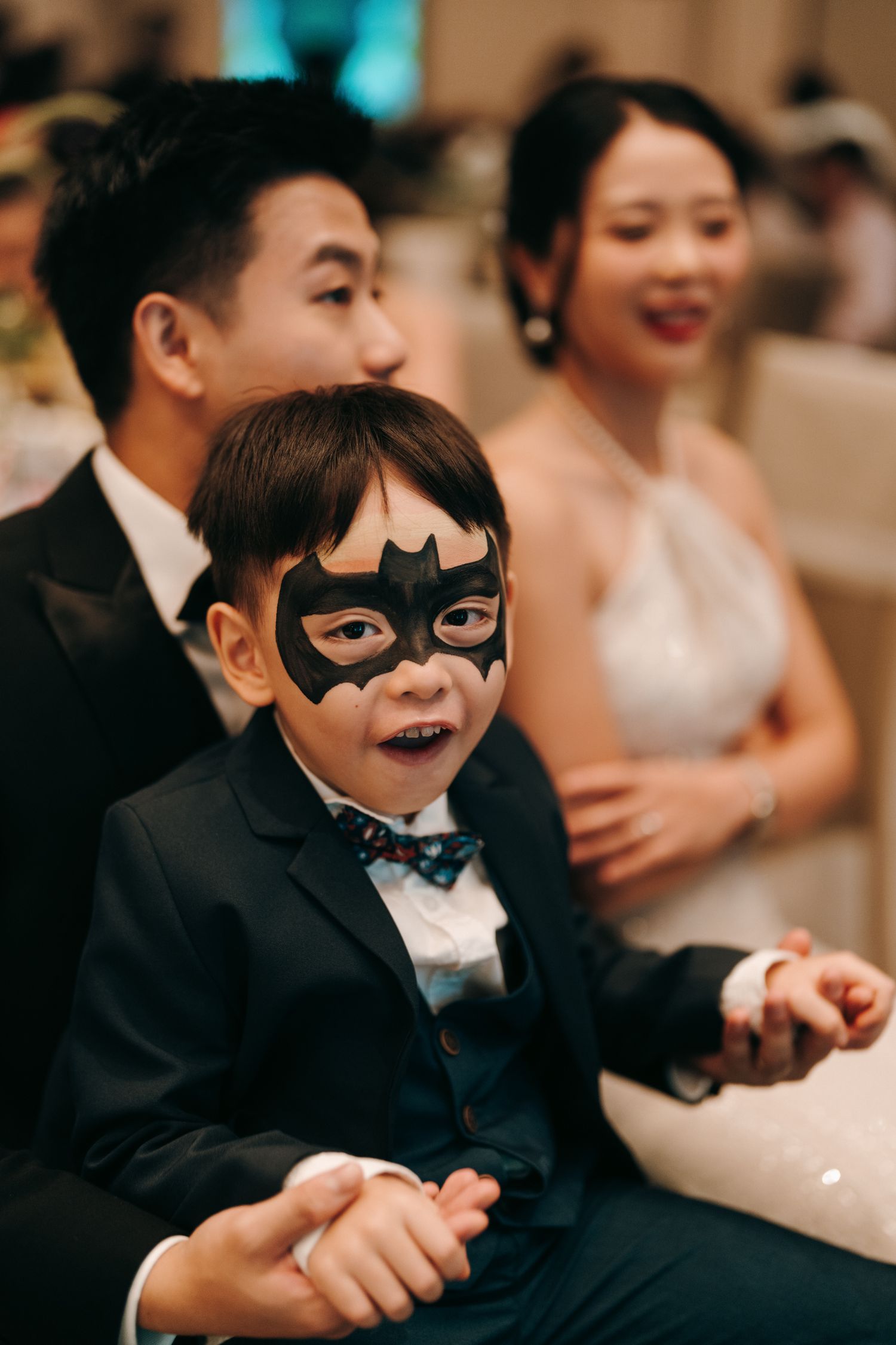 Young ring bearers wearing Batman masks smile and laugh during a wedding reception.