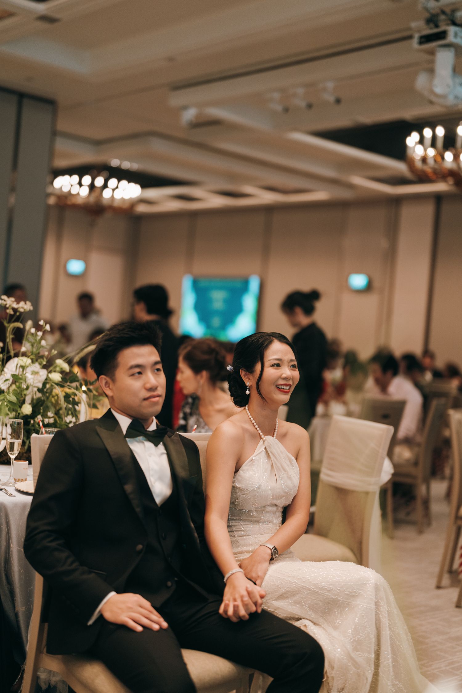 Elegant wedding reception venue with couples seated at tables in a brightly lit ballroom with chandeliers.