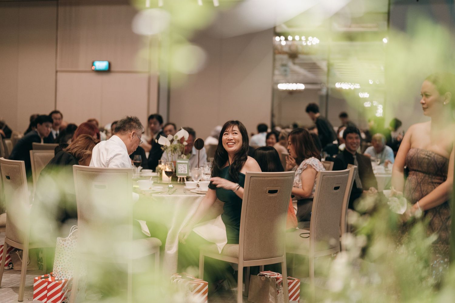 Wedding reception guests seated at round tables in an elegant banquet hall with white decor and floral arrangements.