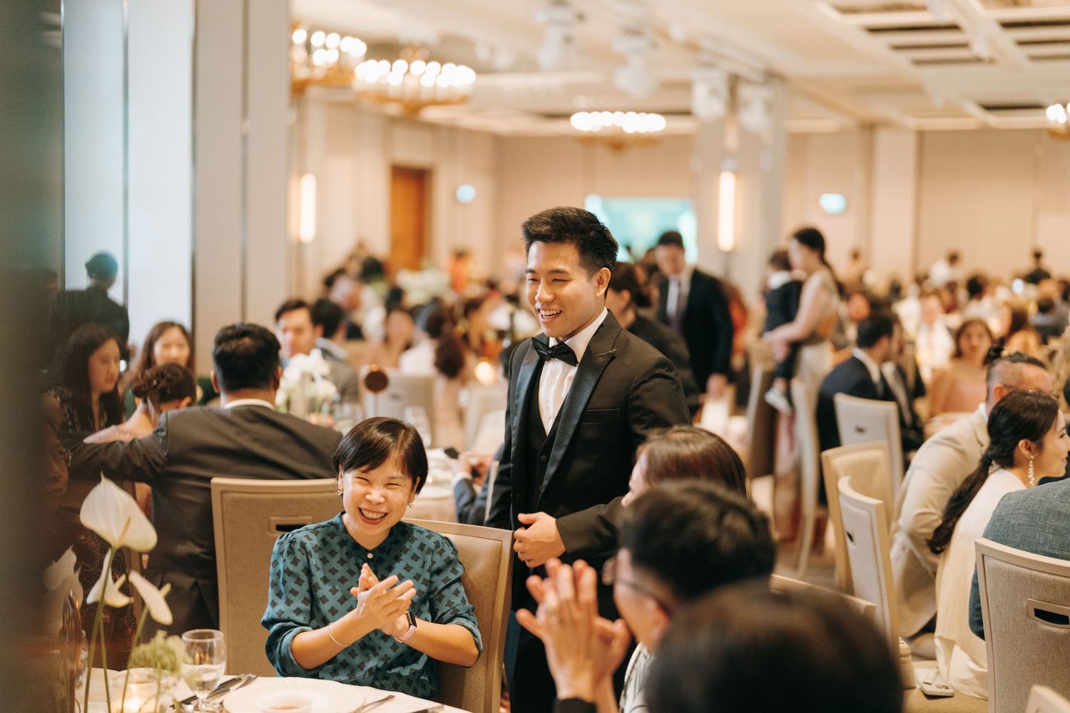 Wedding reception guests applaud during celebrations in a brightly lit banquet hall.