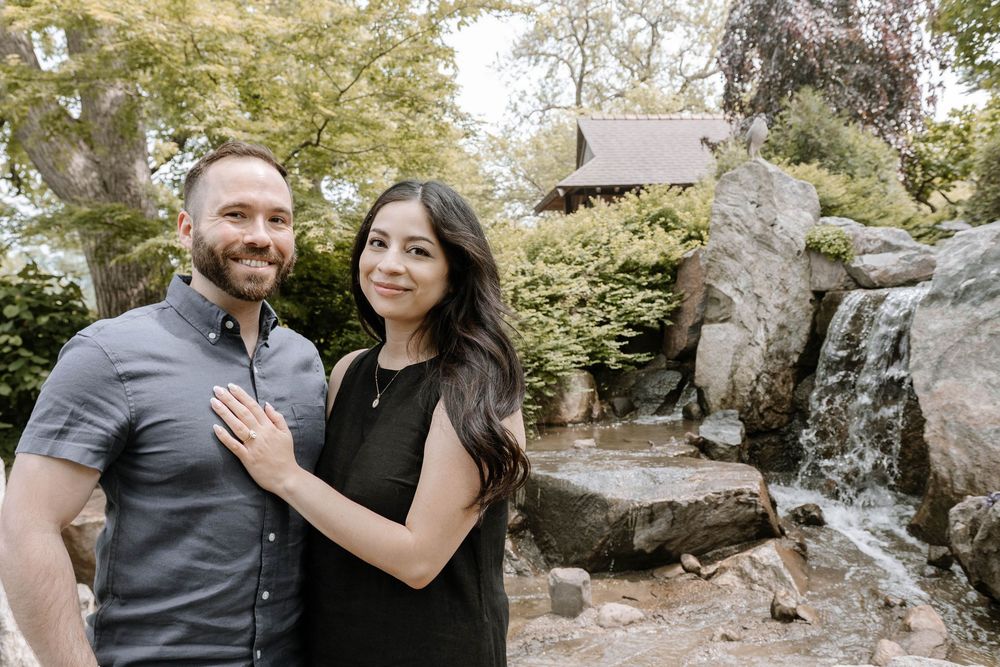 A couple poses together in a scenic outdoor setting with trees and rocks in the background.