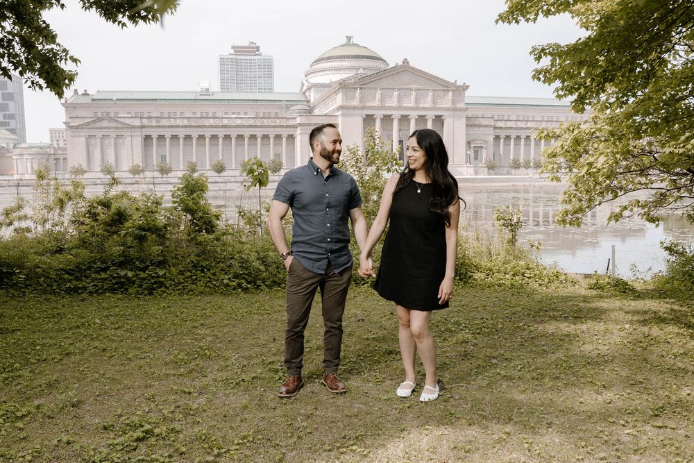A couple walks and poses together on a grassy hill with the U.S. Capitol Building visible in the background.