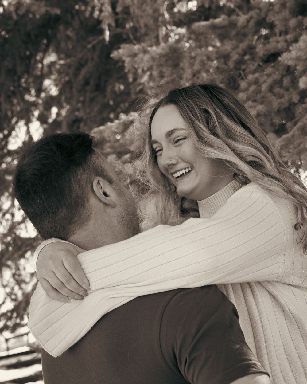 Black and white photo of a smiling woman hugging her partner during an engagement session.