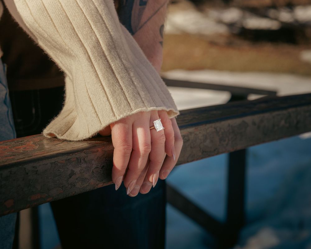 Close-up of a woman's hand displaying a sparkling engagement ring while resting on a railing.