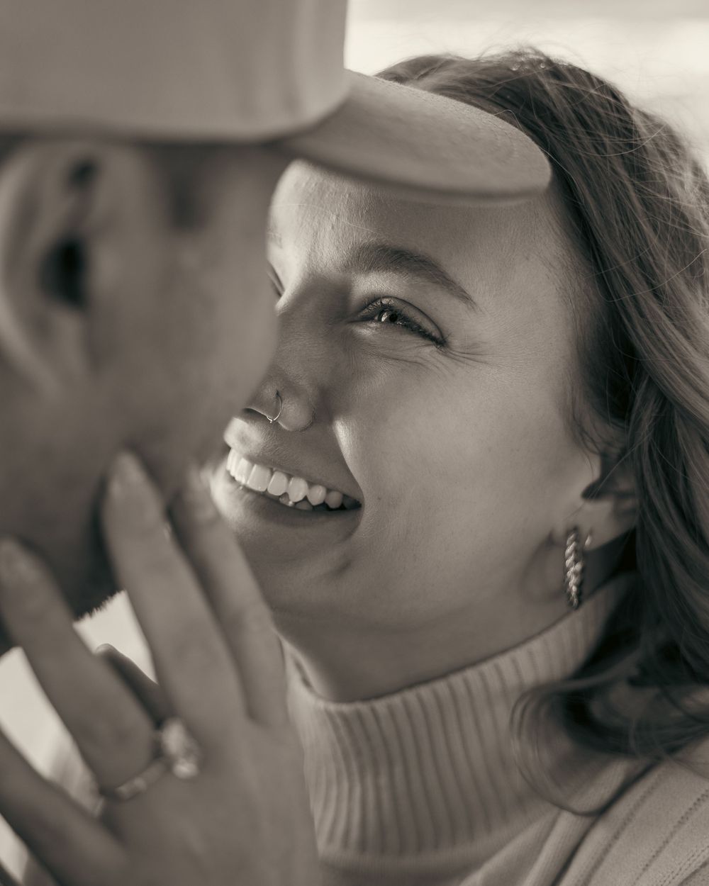 Black and white close-up of a smiling woman showing her engagement ring near her partner's face.
