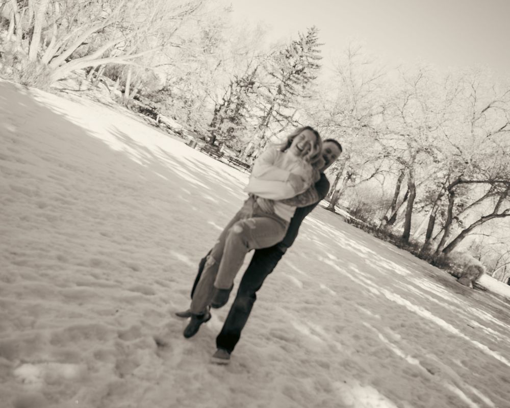 Black and white photo of a man lifting and spinning his laughing partner in a snowy field.