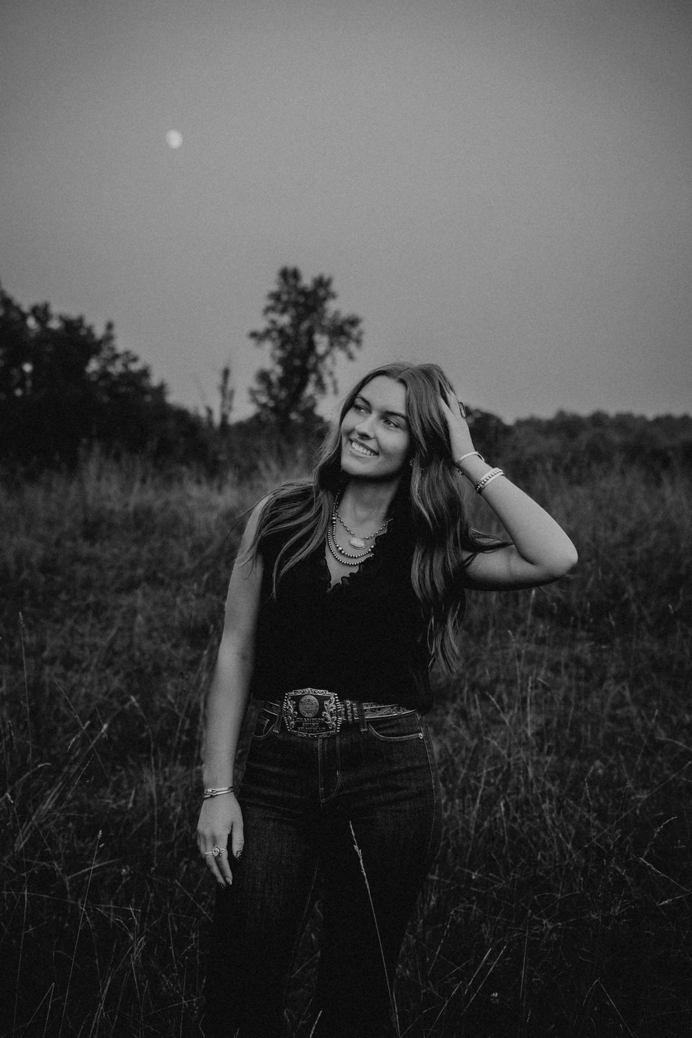 Black and white portrait of person lounging in grassy field at dusk.