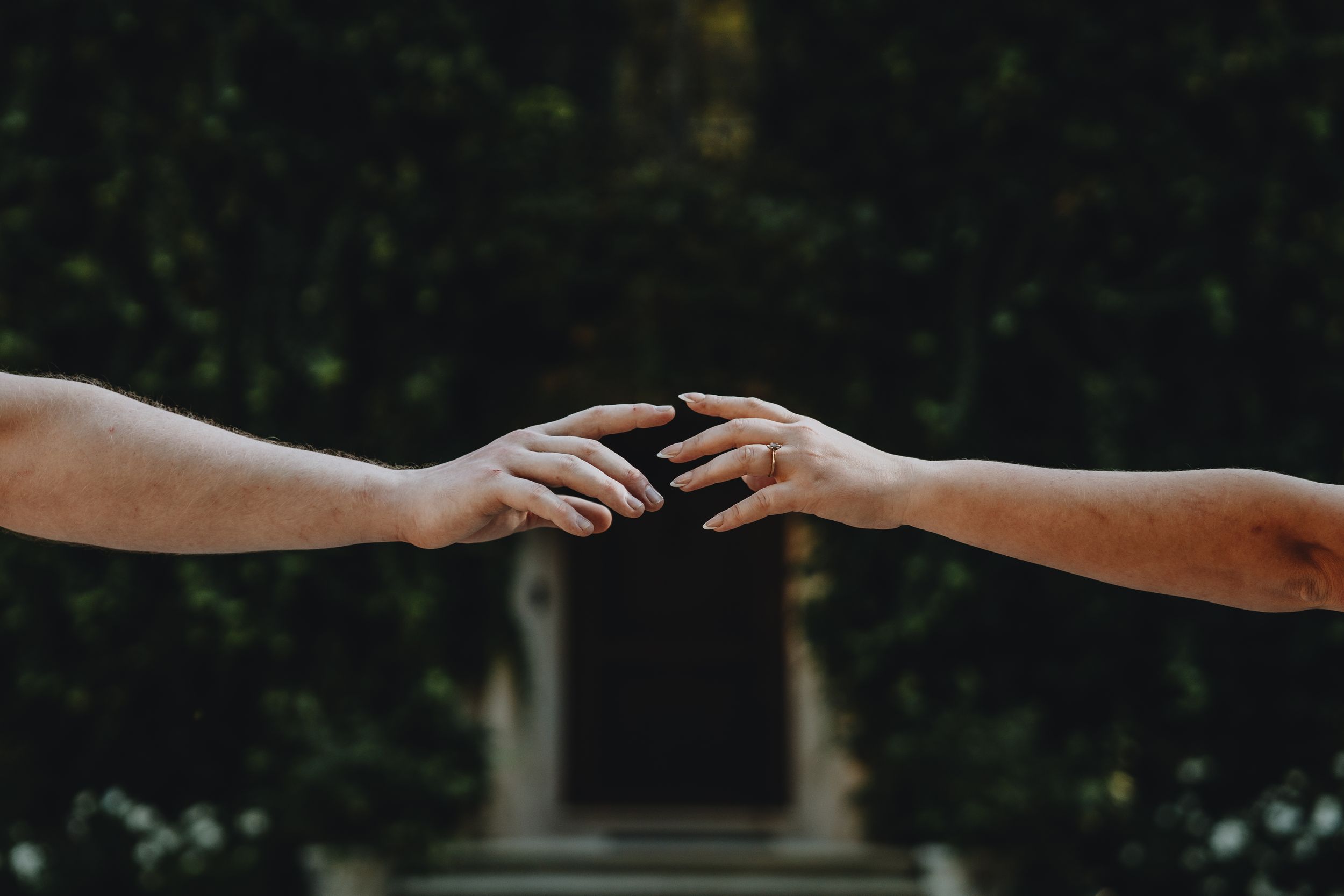 Silhouetted hands reaching towards each other against a dark background.