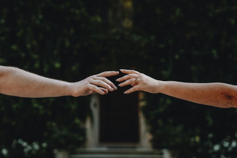 Silhouetted hands reaching towards each other against a dark background.