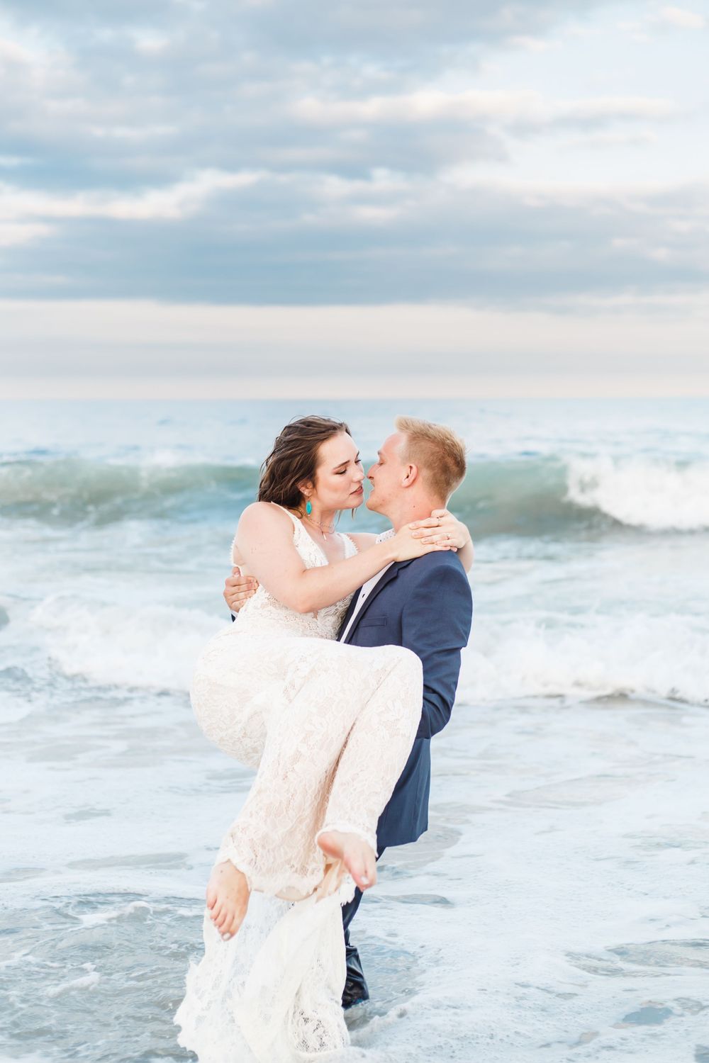 Couple sharing intimate moments by the ocean waves in light colored wedding attire.