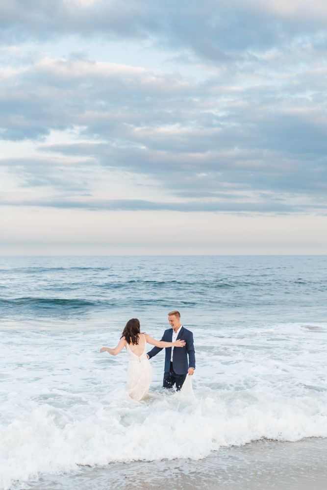 A couple splashes and plays in the ocean waves during their beach wedding photoshoot.