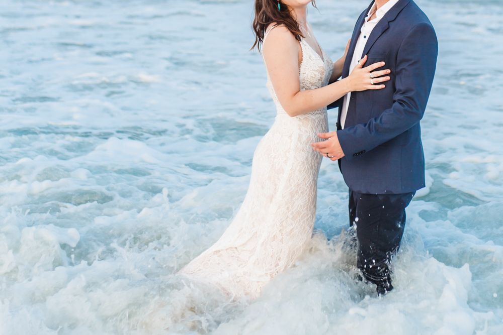 Ocean waves splash around a couple during a beach engagement photo session.