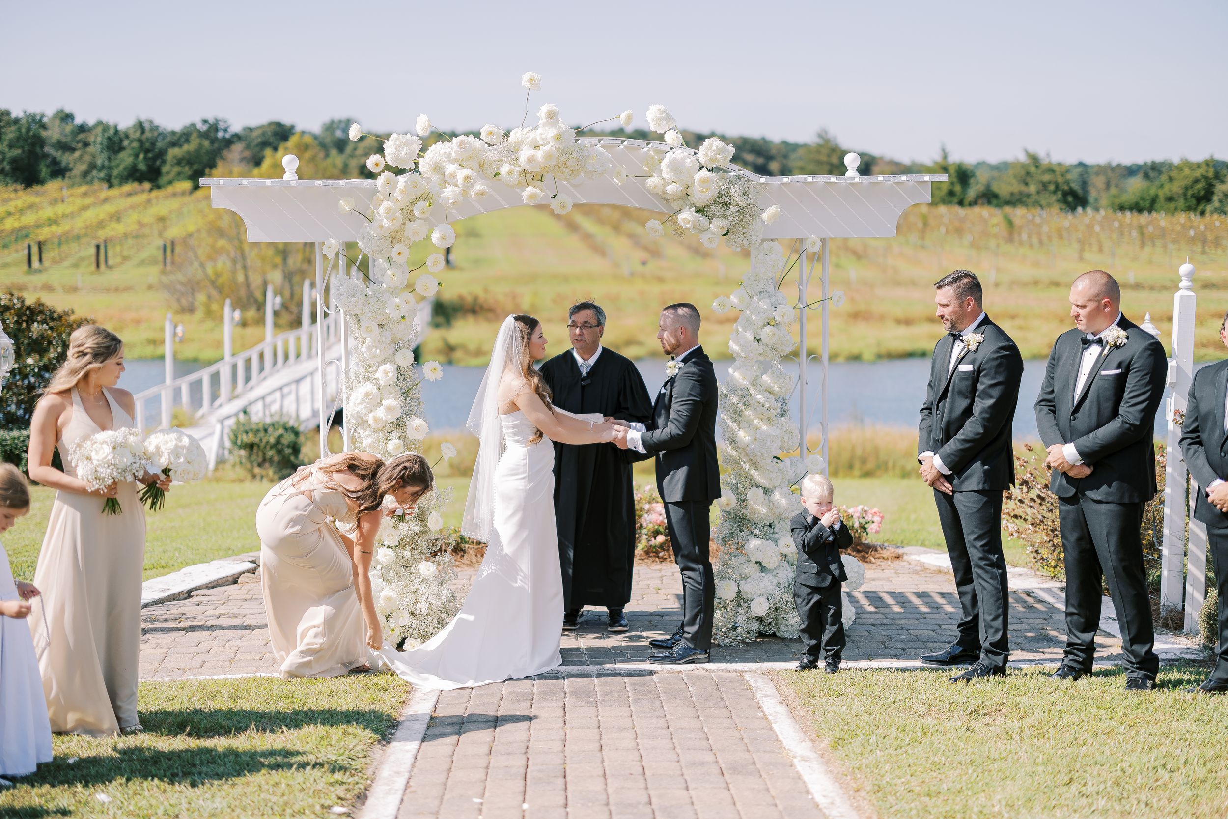 Panoramic view of an outdoor wedding ceremony setup with white picket fencing and floral decorations by the water.