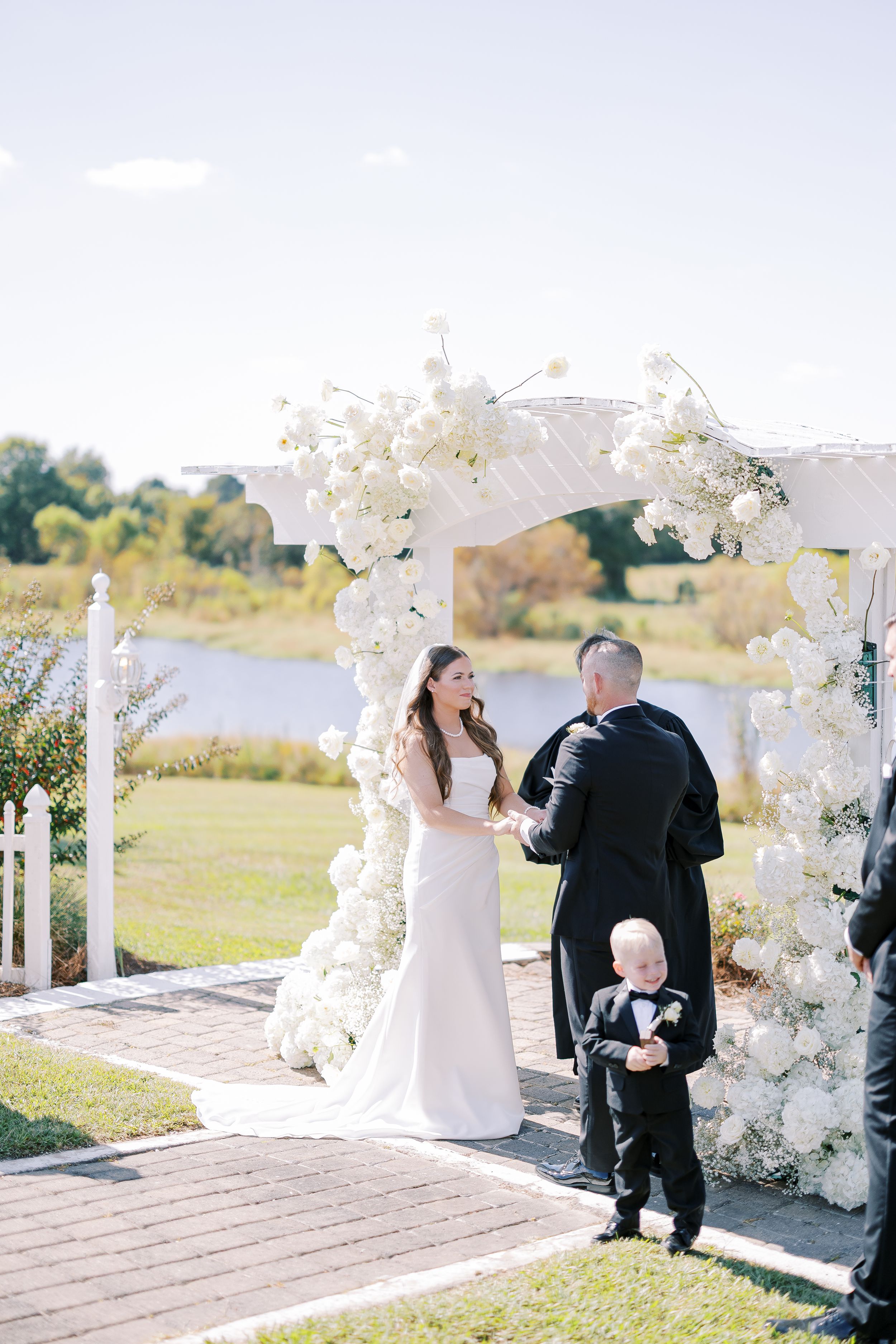 A sequence of five outdoor wedding ceremony photos with white floral arch decorations by a waterfront.