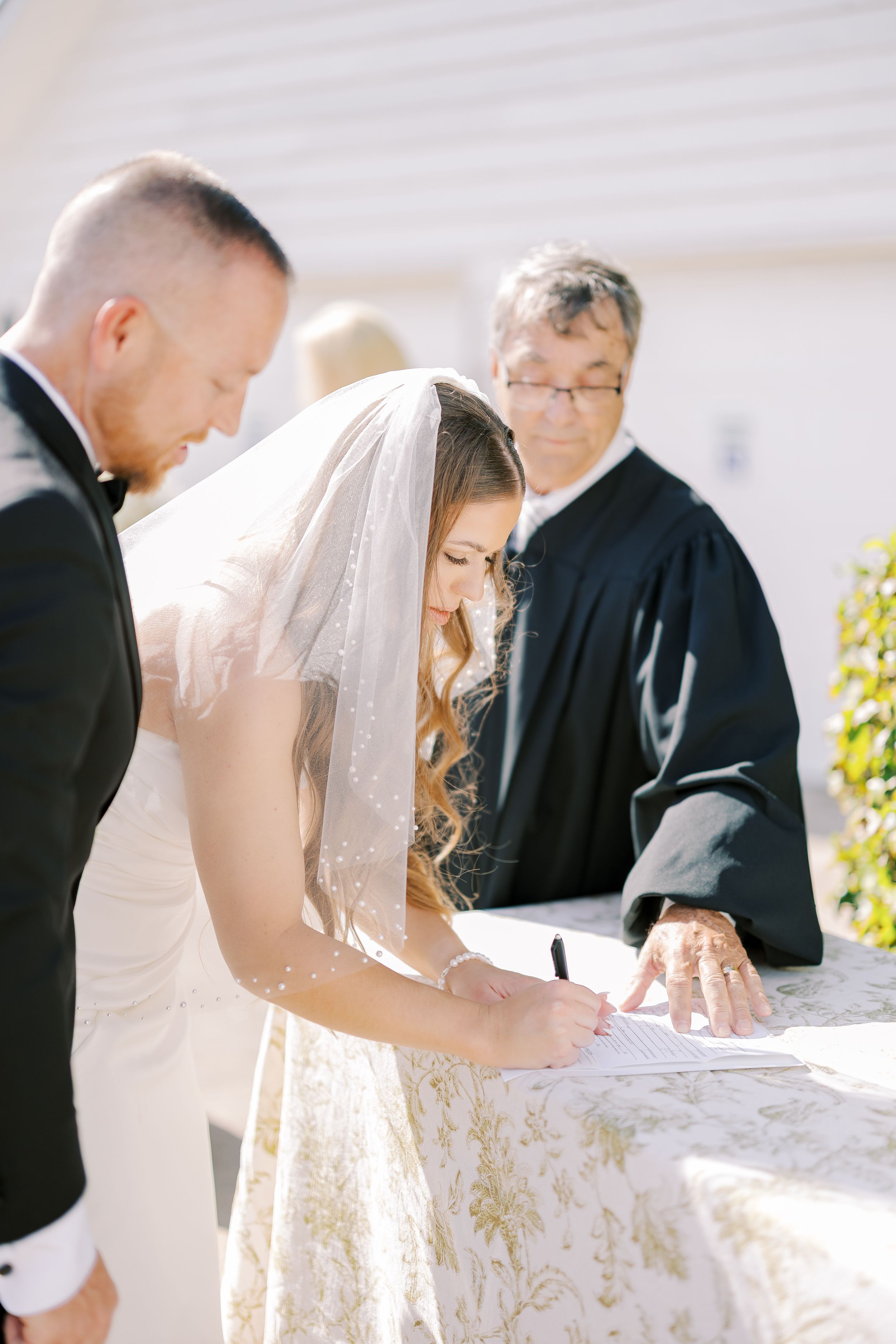 A couple signing their wedding ceremony documents at an outdoor venue in bright sunlight.