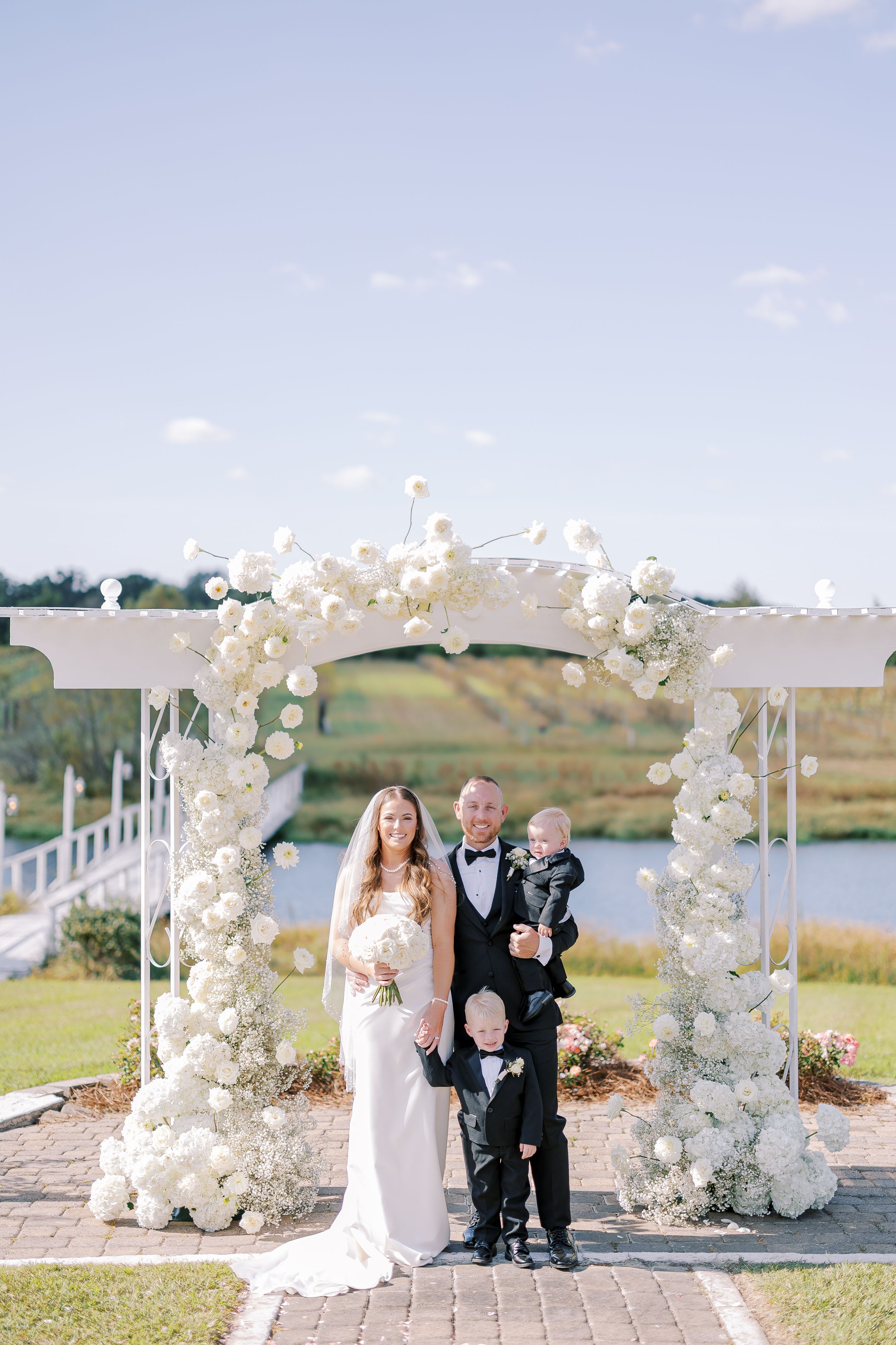 Outdoor wedding ceremony setup with white floral arch and pathway overlooking scenic countryside landscape.