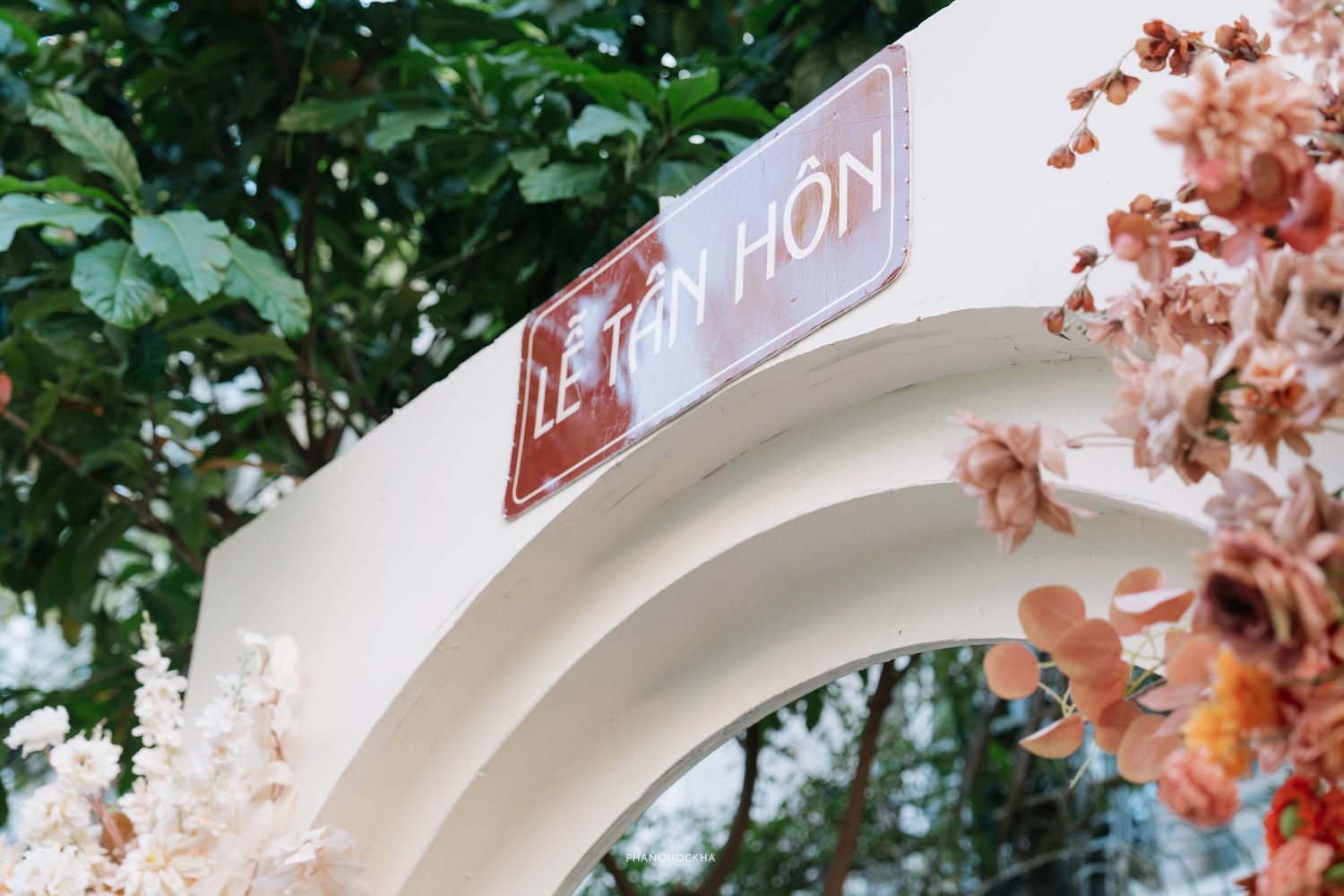 Close-up of white arch sign reading Le Tan Hon decorated with pink and white blossoms.