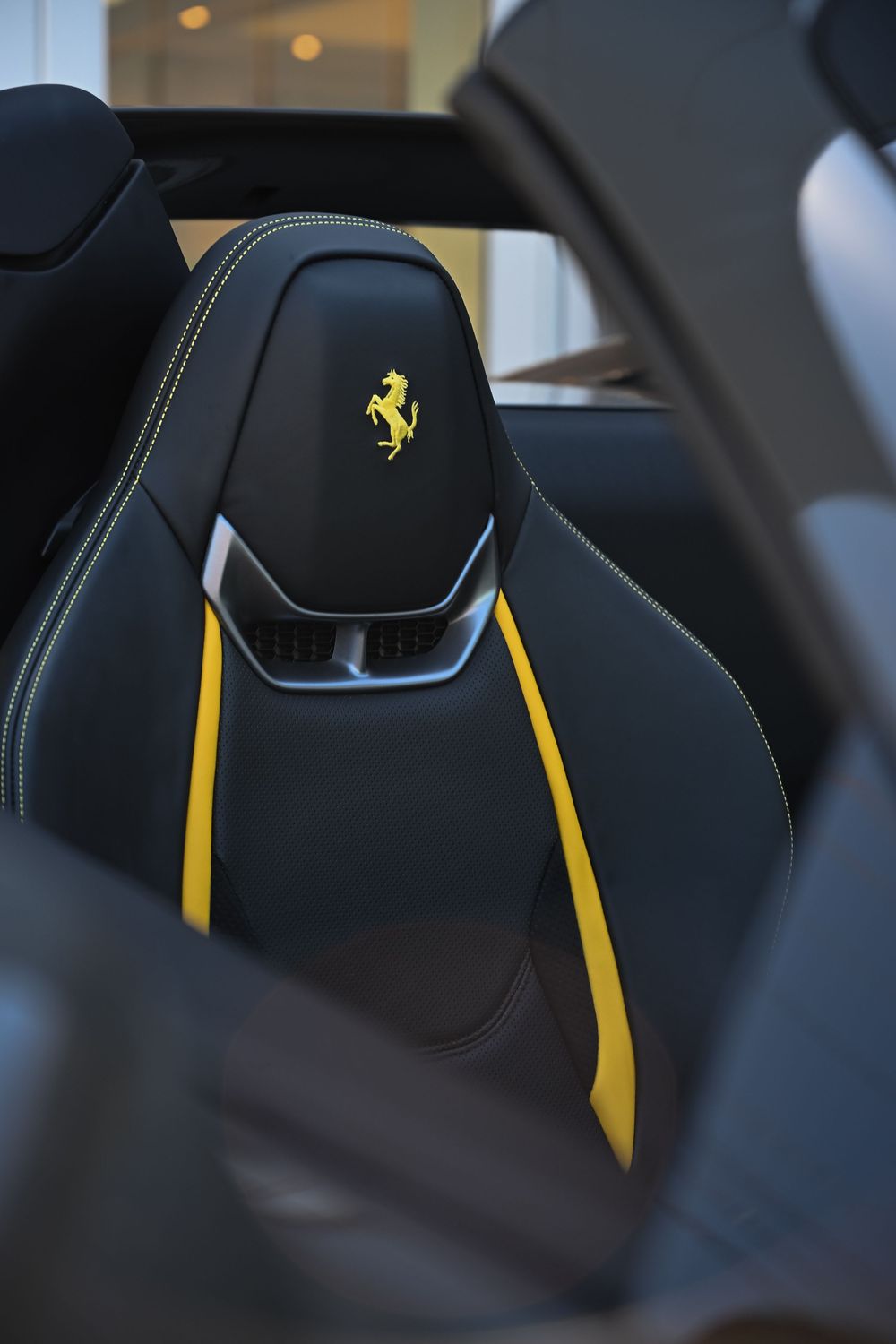 Detail shots of black luxury car seat with yellow Ferrari logo and accent stripes in leather upholstery.