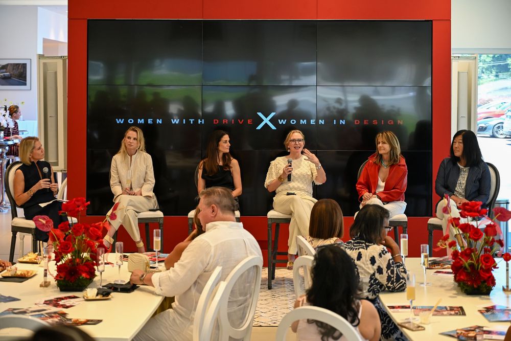 Business professionals gathered around conference tables in a modern office space with red wall accents.