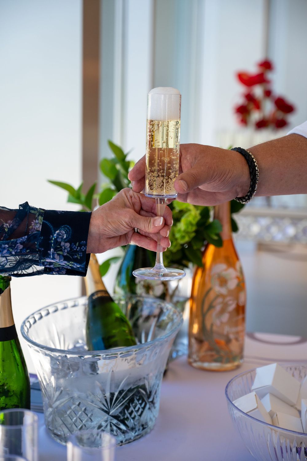 Hand pours sparkling wine into crystal glass at an elegant table setting with decorative details and white décor.