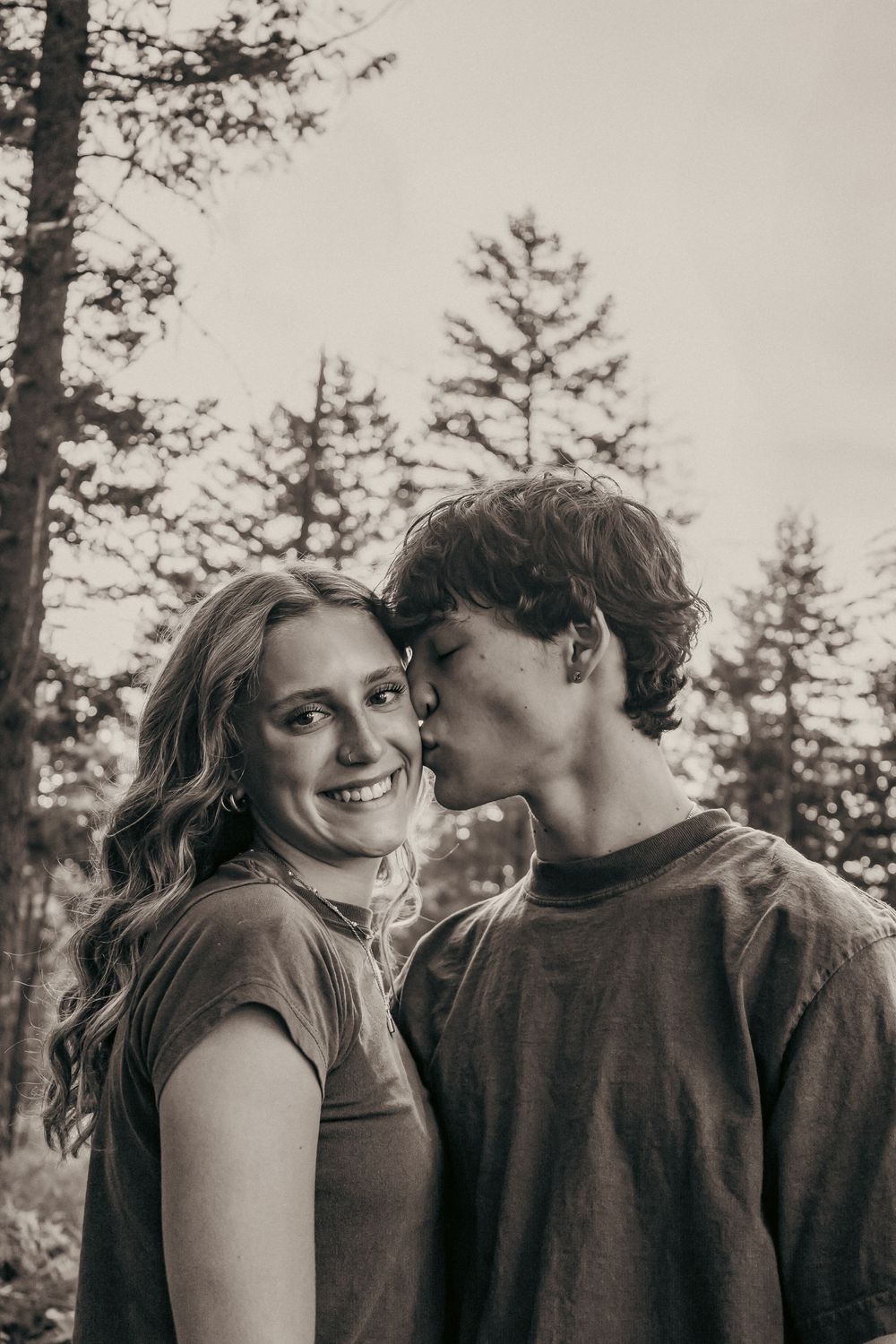 Black and white portrait of couple sharing tender moment among pine trees.