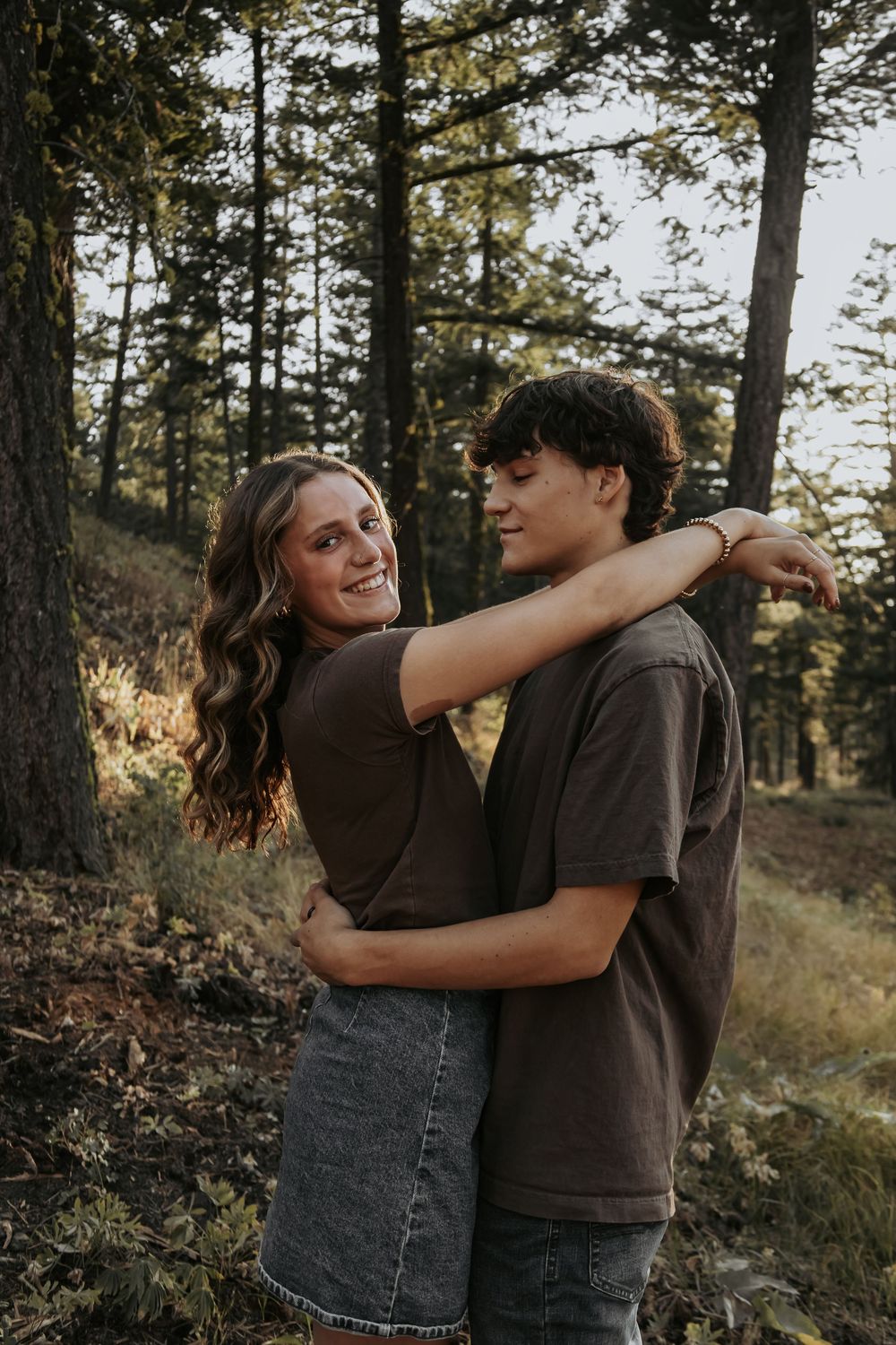 A couple embraces and laughs together in a forest setting during sunset.