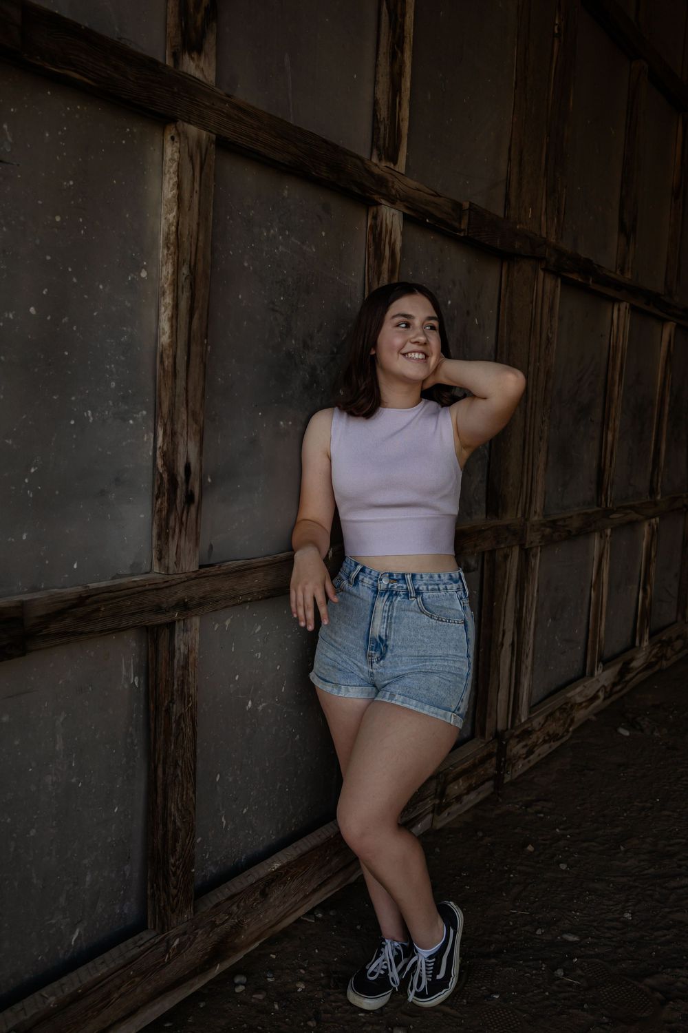 Moody portrait series against rustic wooden wall wearing light top and denim shorts.