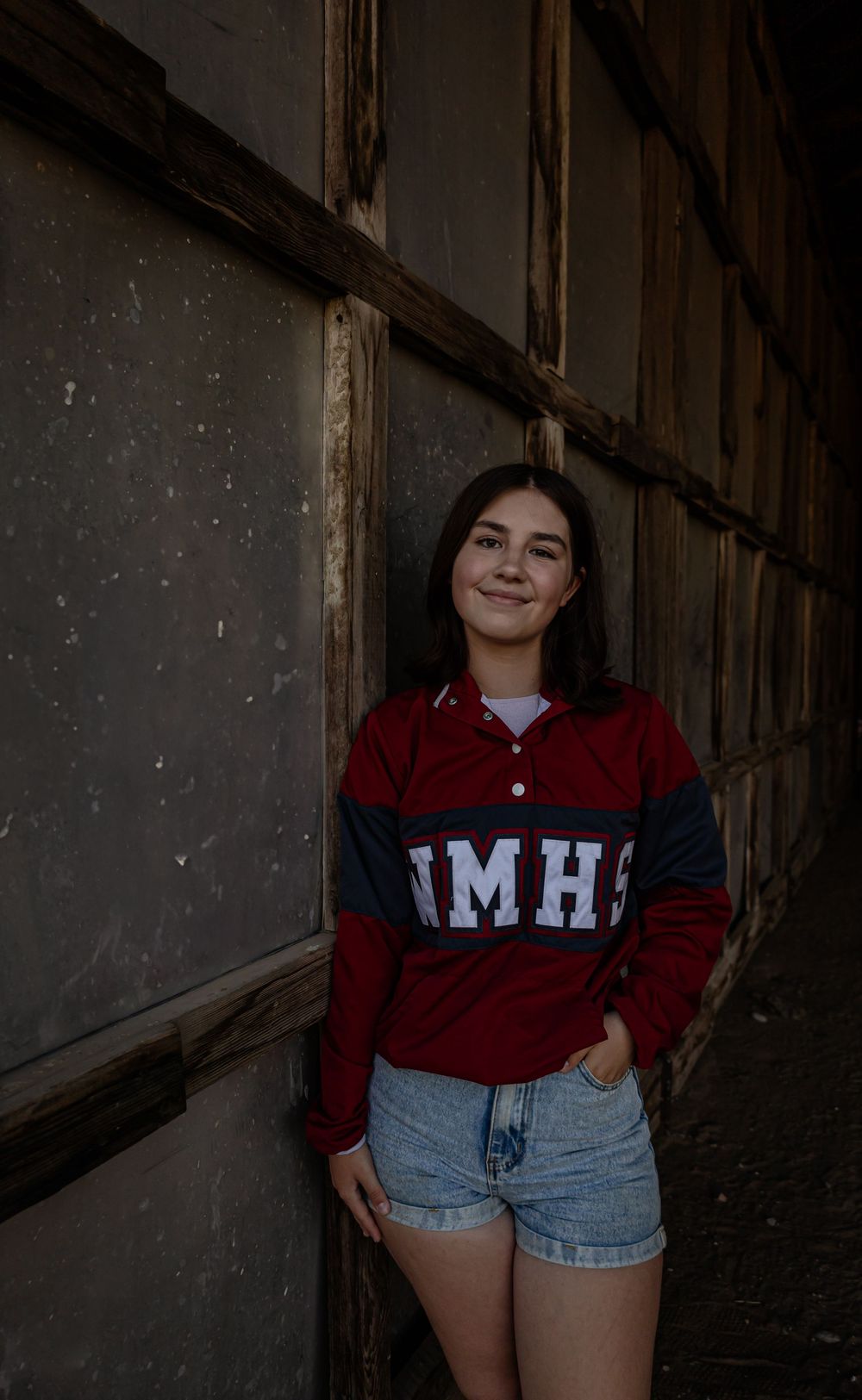 Fashion portraits in maroon collegiate sweater and denim shorts against industrial backdrop.