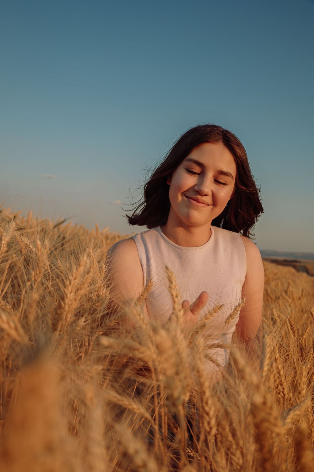 Sunset portraits in wheat field wearing white sleeveless top with golden hour lighting.
