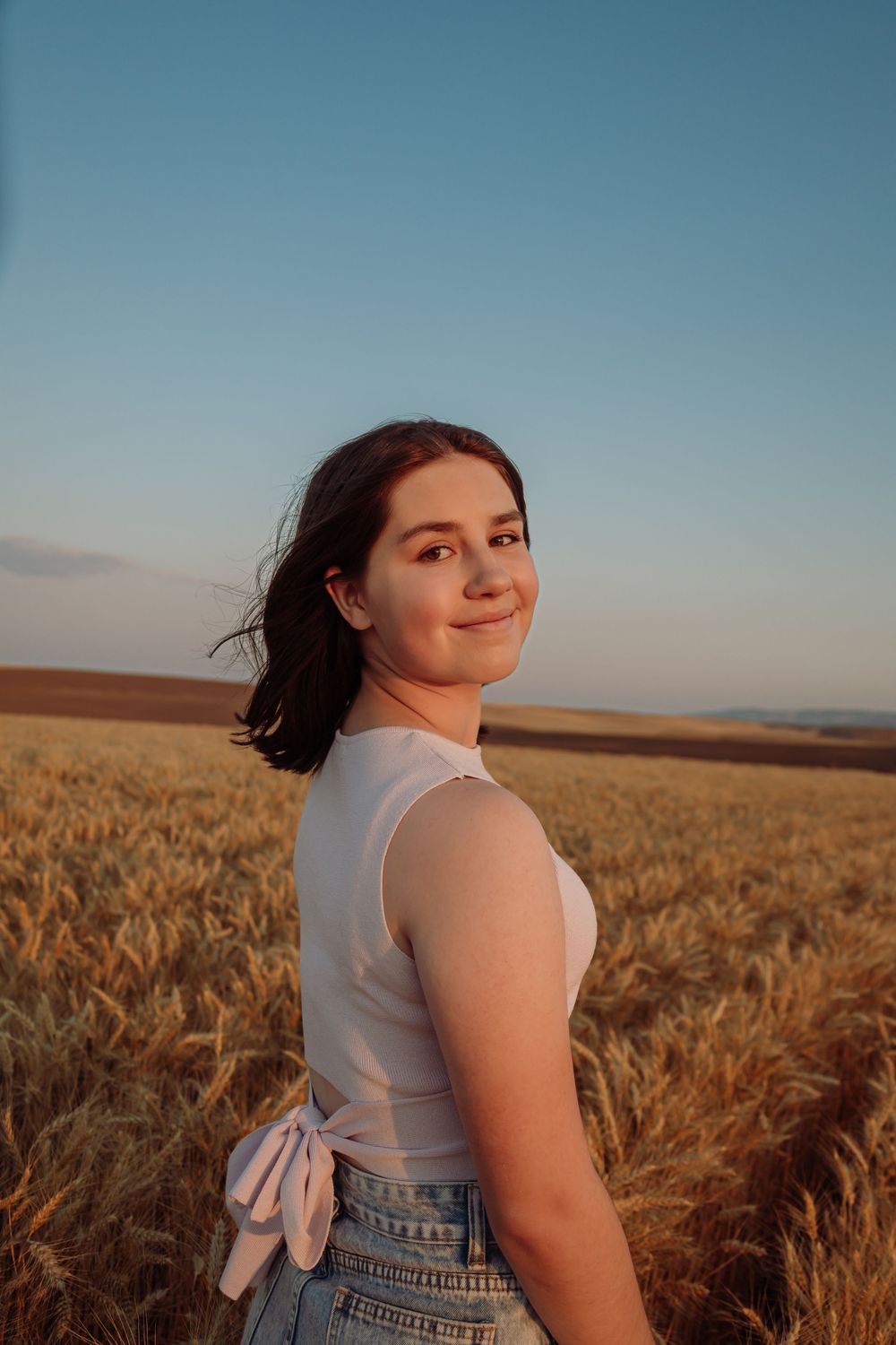 Golden hour portraits in wheat field wearing white top and denim with bow detail.